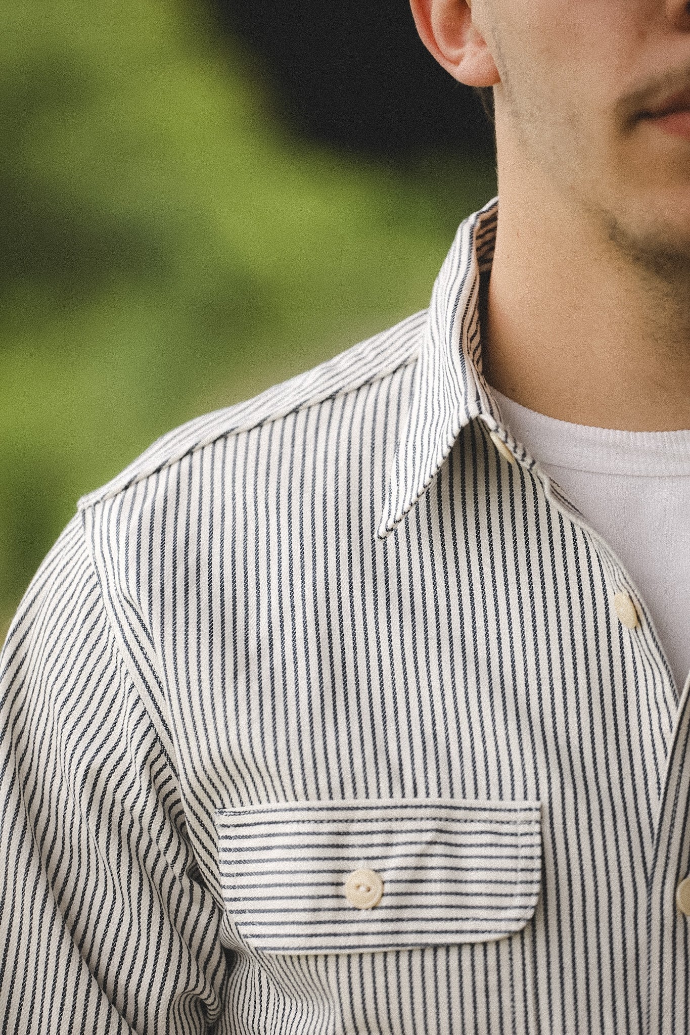 Close-up of a person wearing a striped shirt with a blurred green background