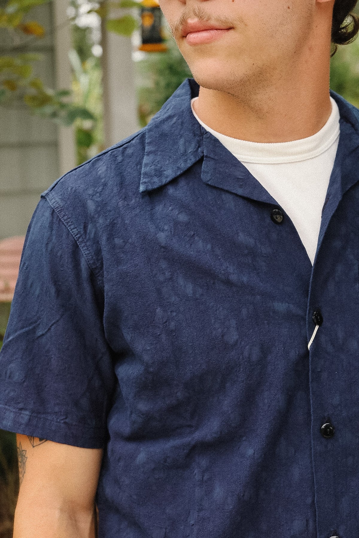 A close-up of a man wearing a navy blue short-sleeve button-up shirt with a subtle mottled texture, layered over a white t-shirt.