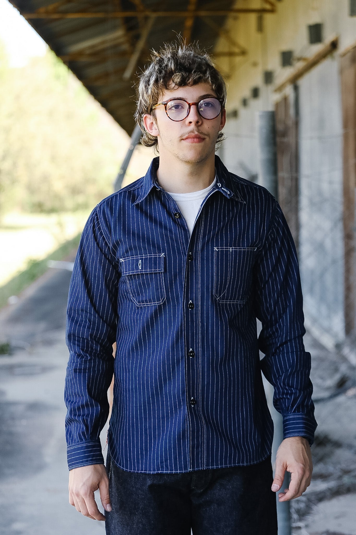 Person wearing a blue striped shirt standing outdoors under a shelter.