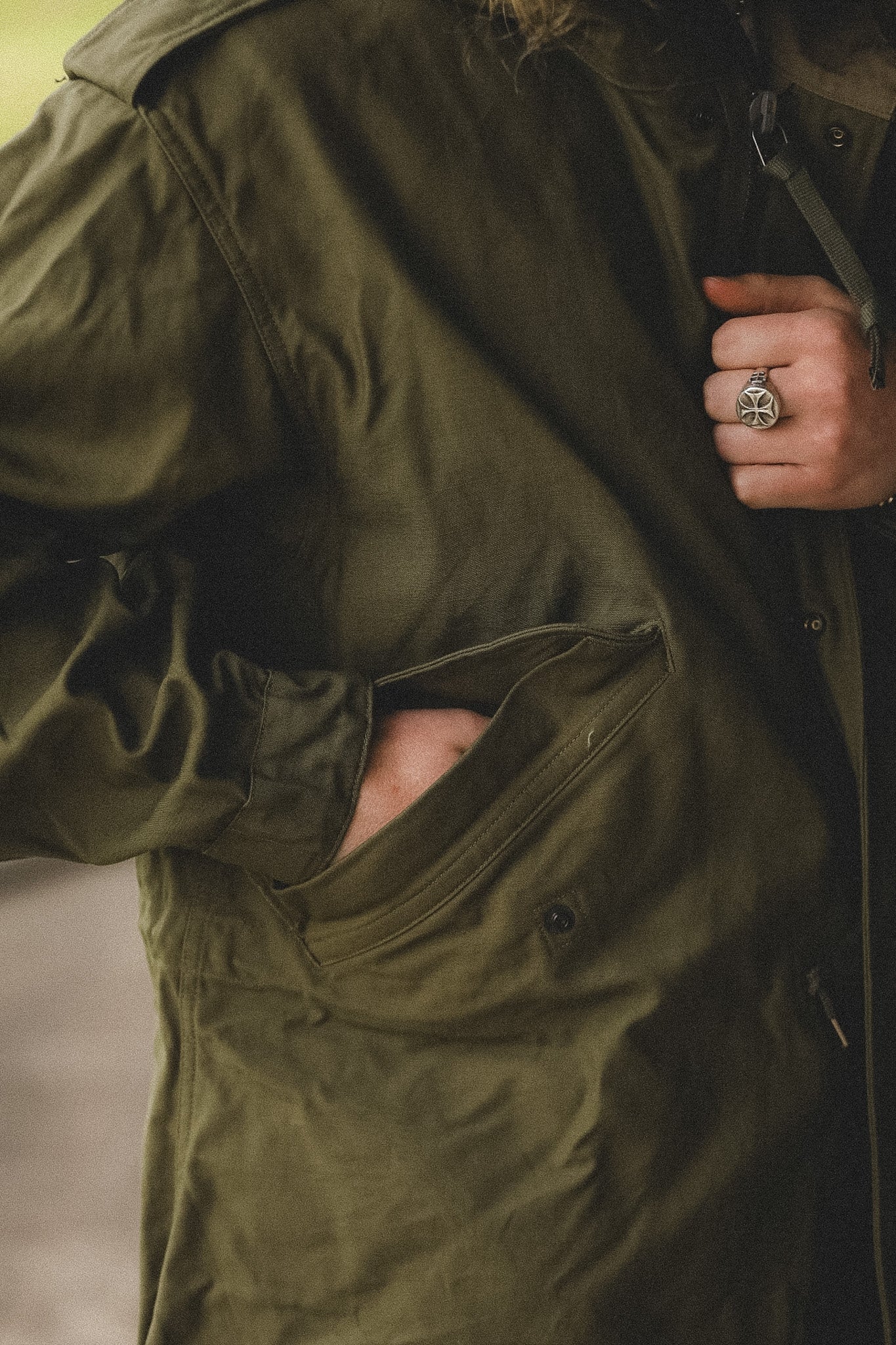 Person wearing a green coat with a close-up of the pocket and hand.