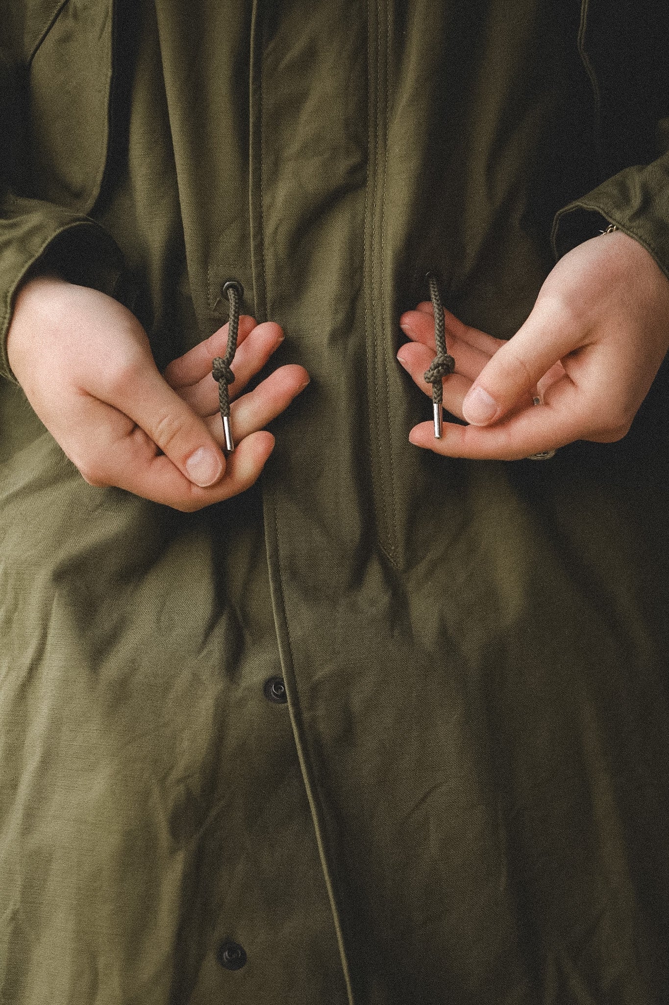 Person wearing a green coat with buttons being adjusted.