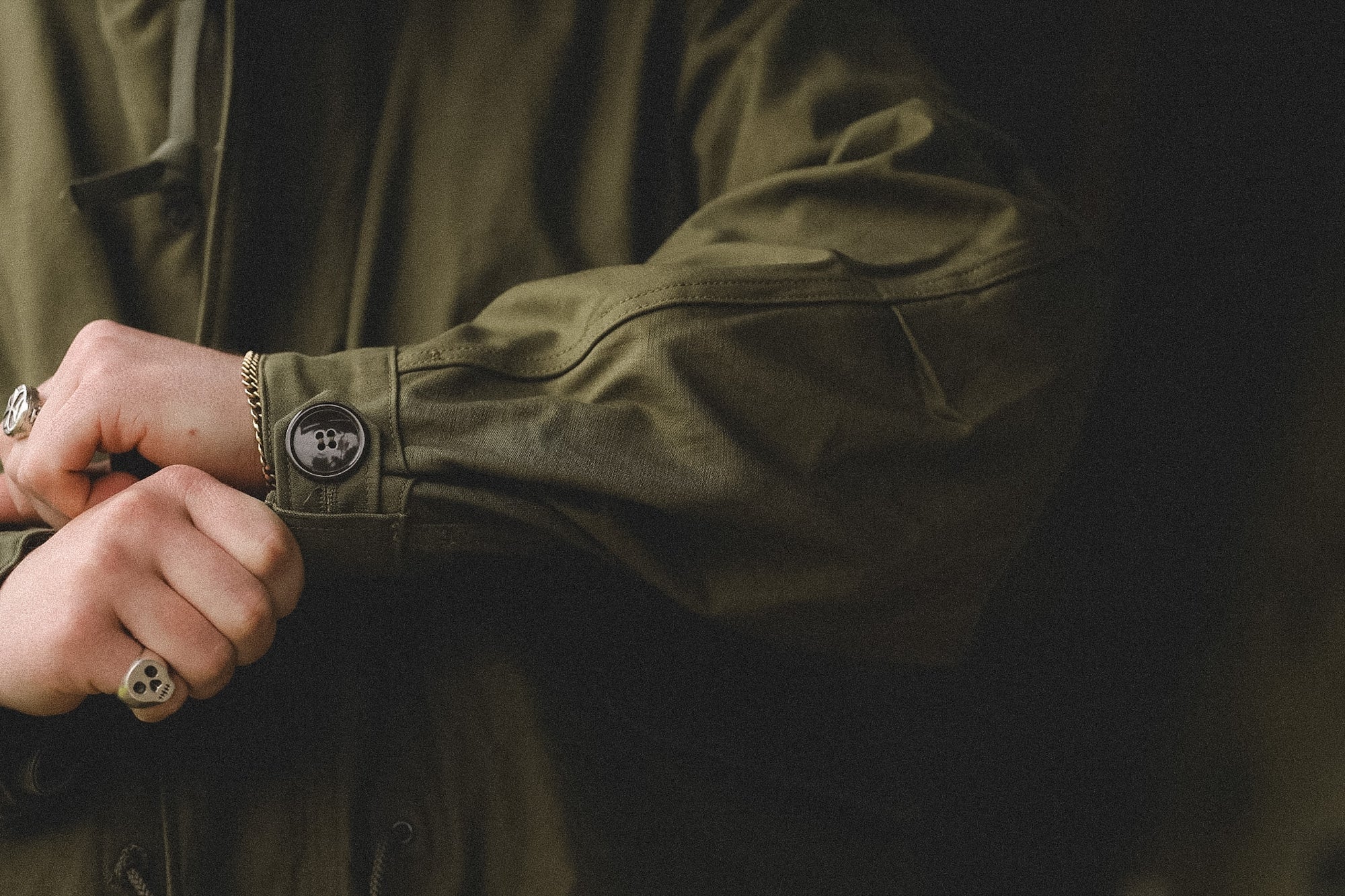 Close-up of a person wearing a green jacket with a button, on a dark background