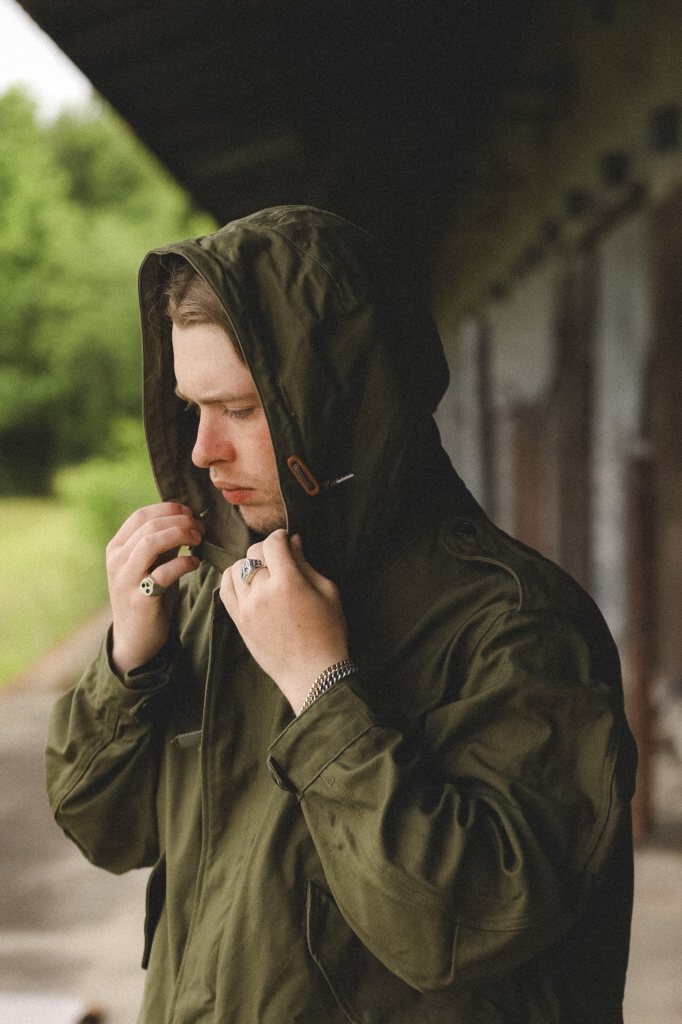Man adjusting his hooded raincoat outdoors with a blurred background