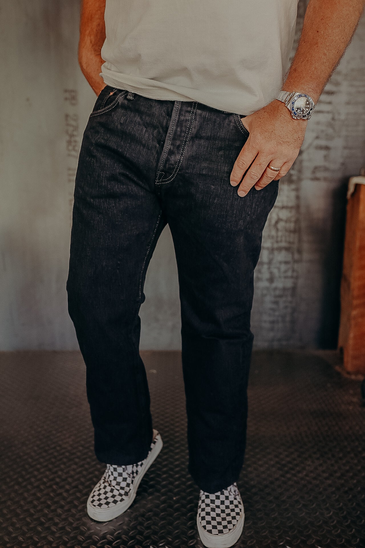 Man wearing black denim jeans and checkered slip-on sneakers indoors on industrial floor