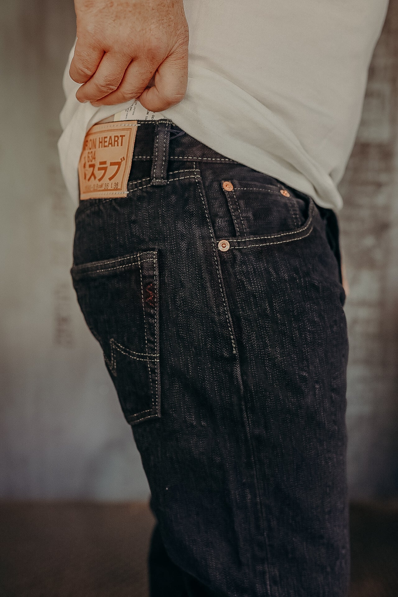 Close-up of person wearing dark iron heart denim jeans with visible leather patch and stitching details