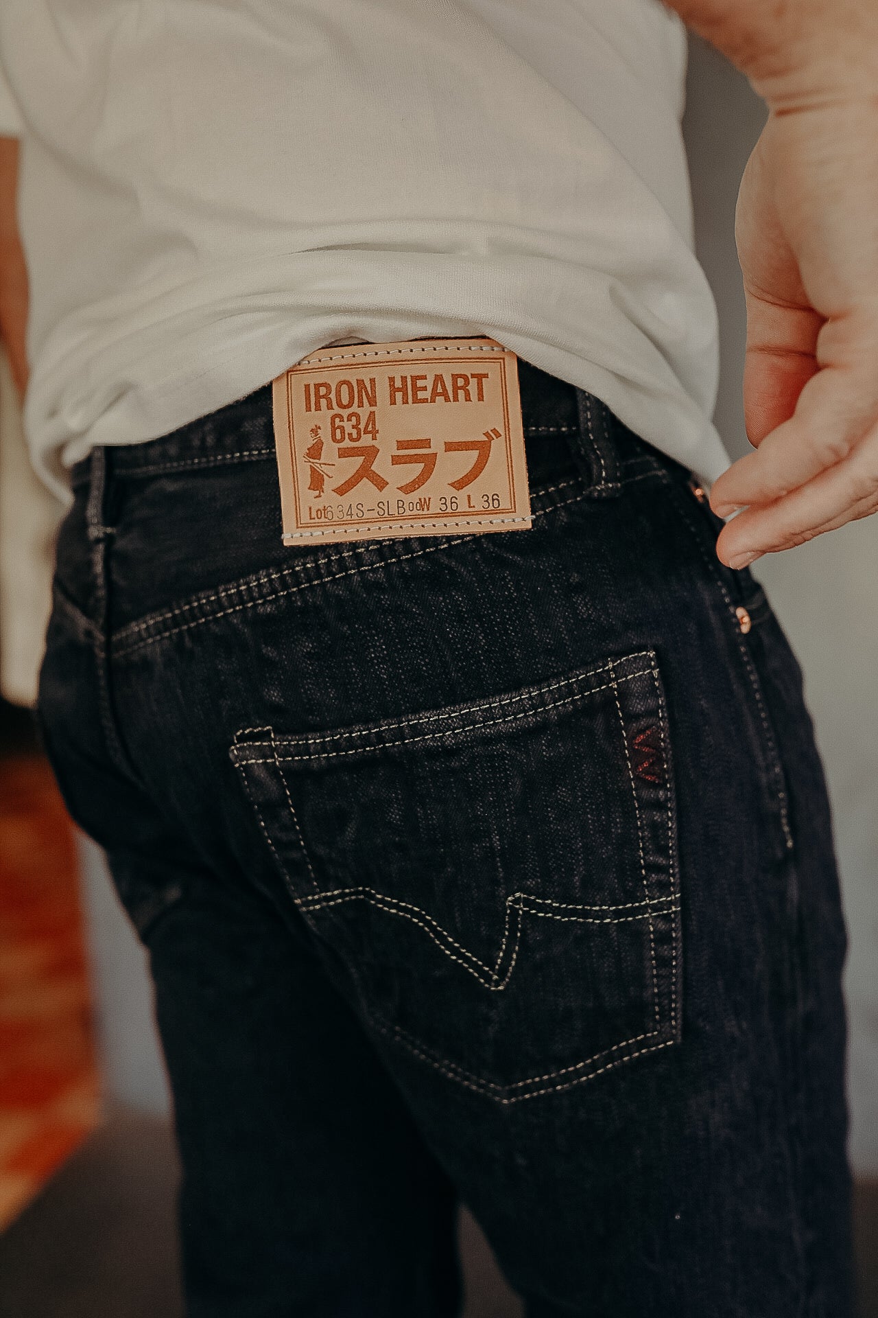 Close-up of black Iron Heart 634 denim jeans with tan leather logo patch and white stitching