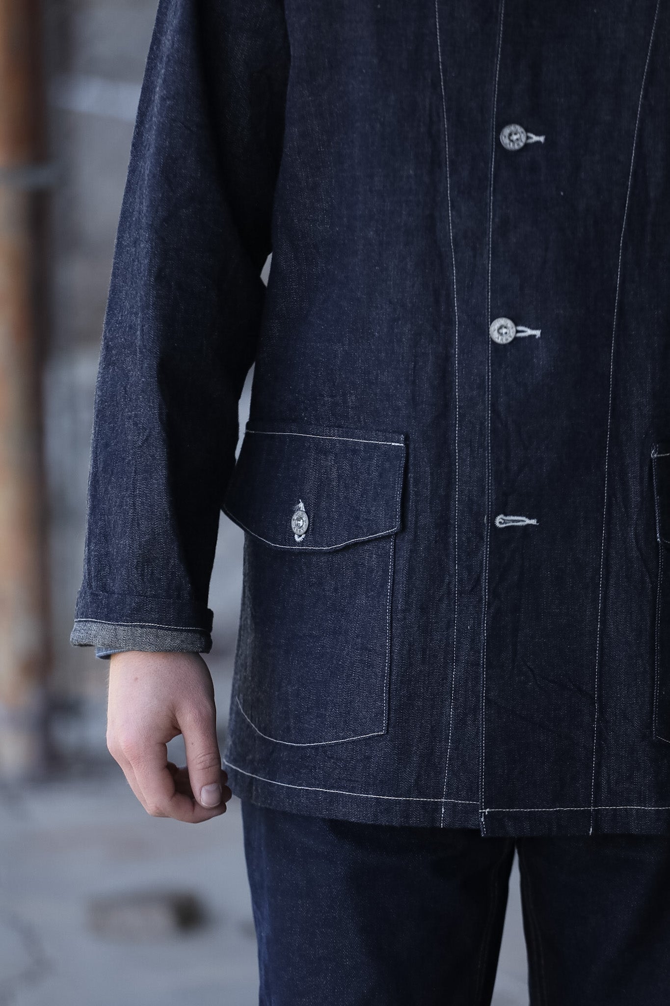 Dark denim coat with button details on a blurred background