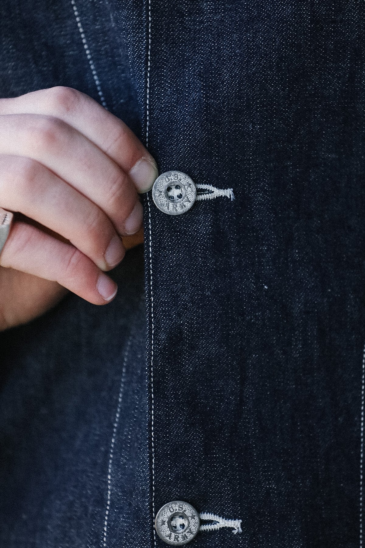 Close-up of a hand buttoning a dark denim jacket with a skull design on buttons.