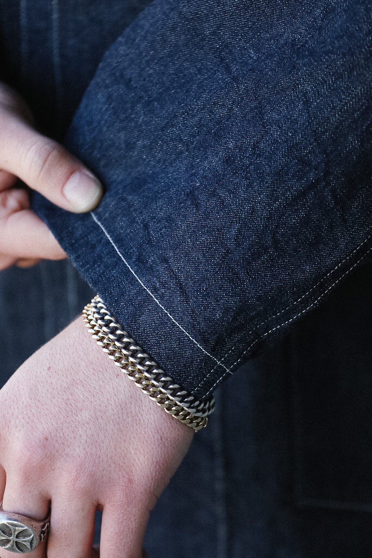 Close-up of a hand wearing a gold bracelet with a dark blue denim sleeve.