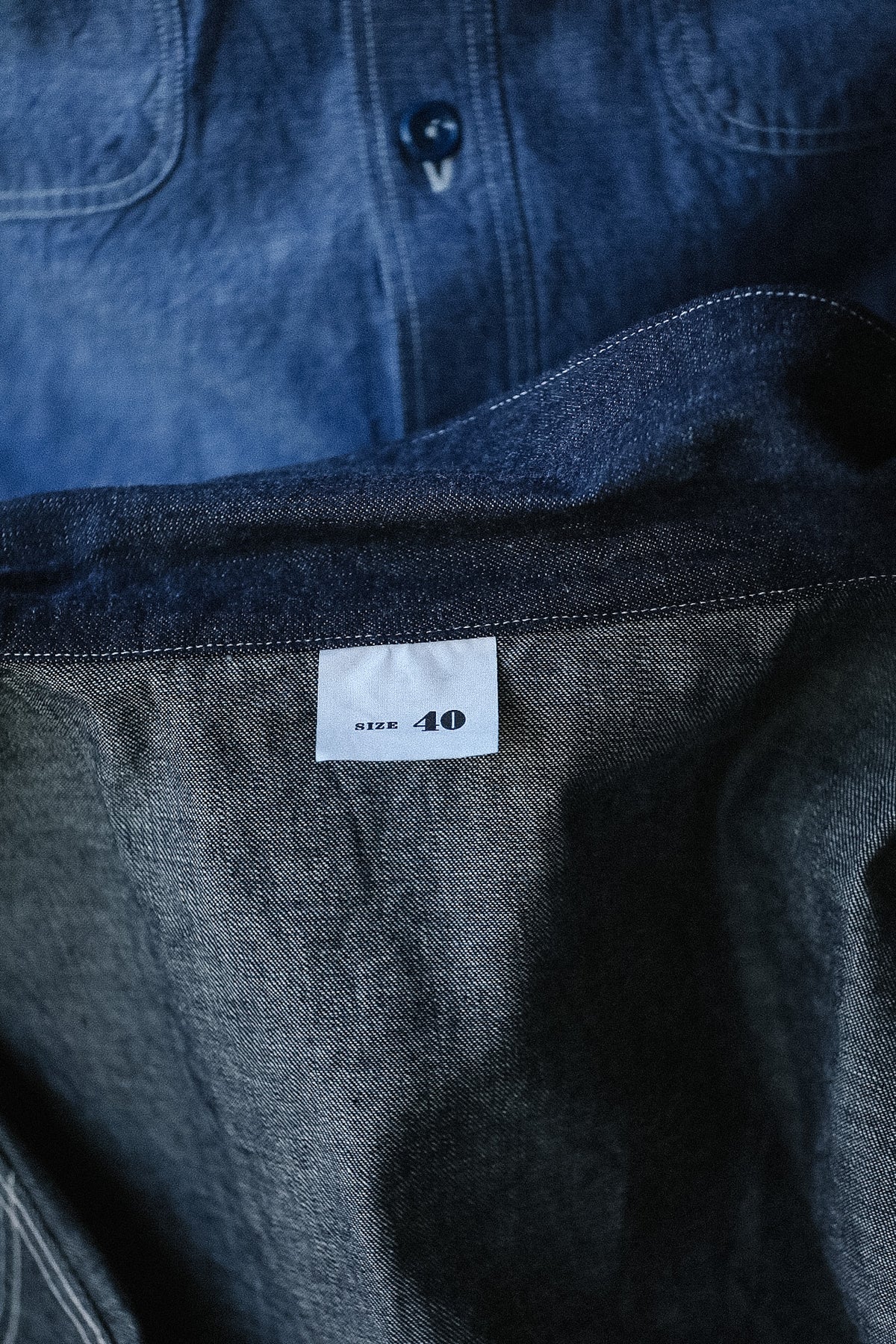 Close-up of a dark denim shirt with a size label on a blurred background