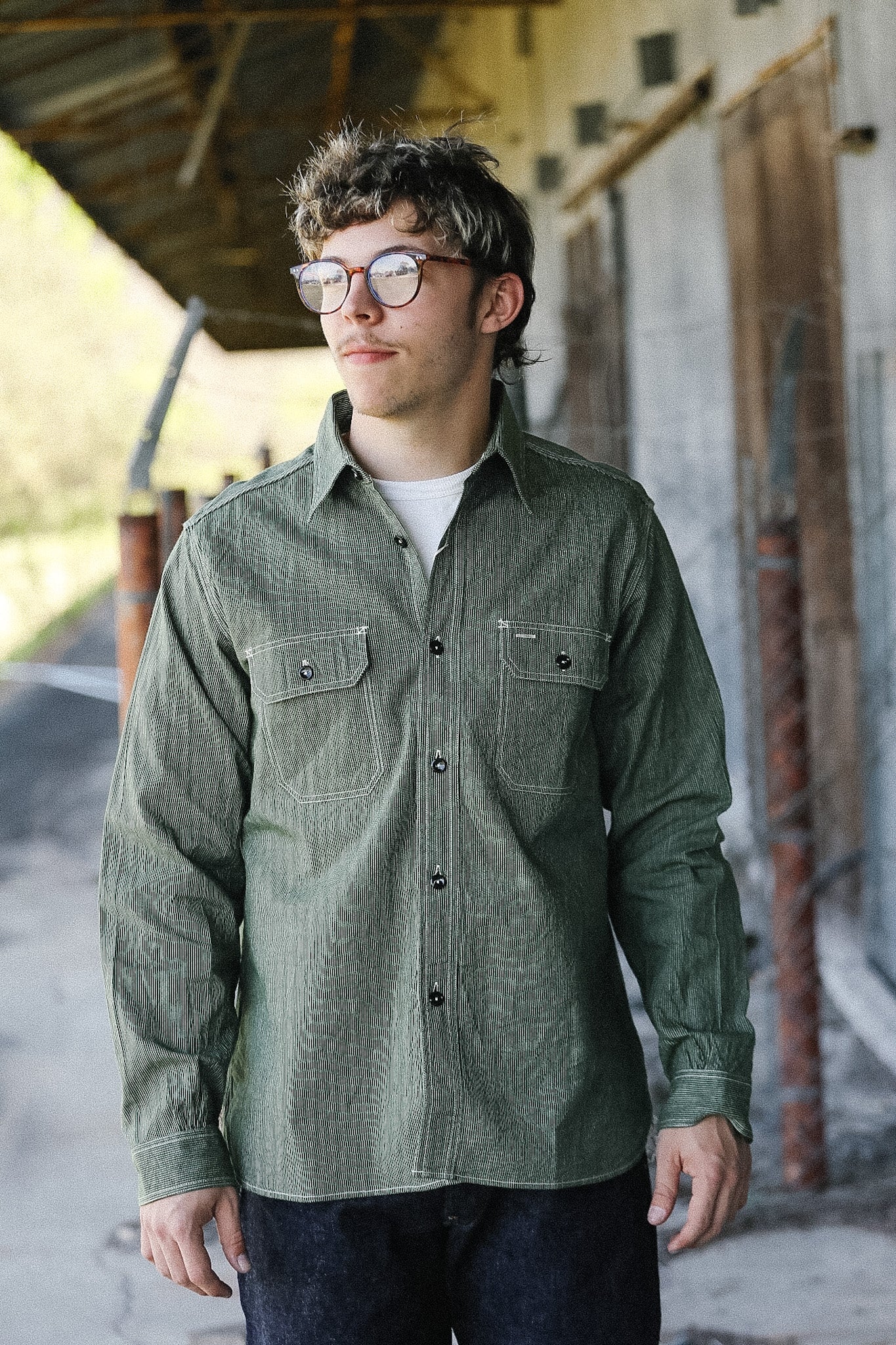Man wearing a green button-up shirt and glasses standing in an outdoor setting.