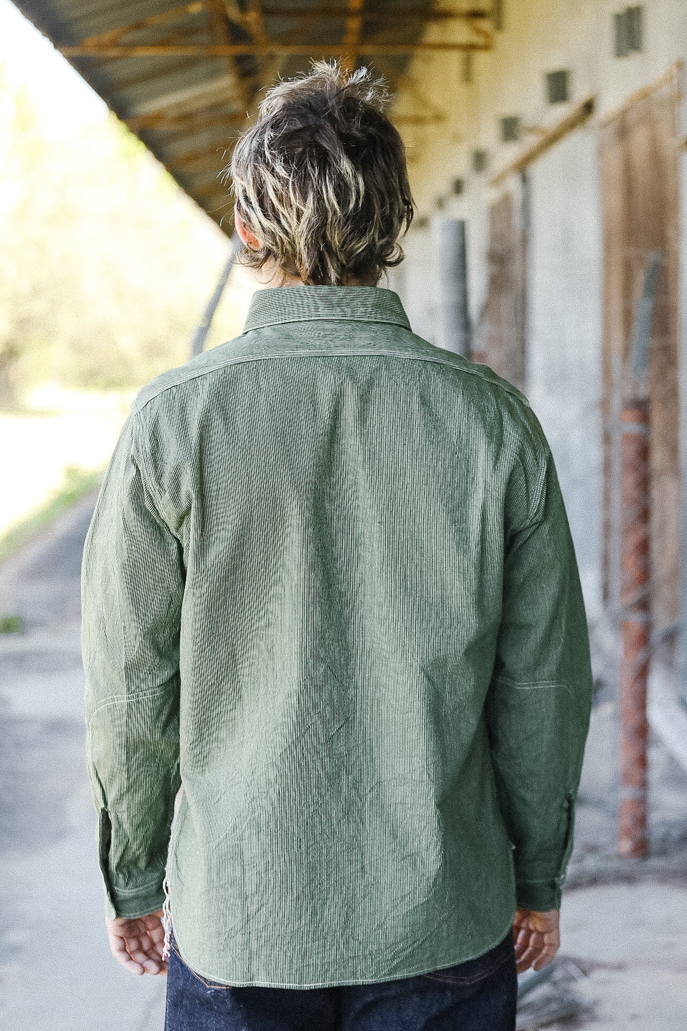 Person wearing a green shirt standing under a covered area with a blurred background