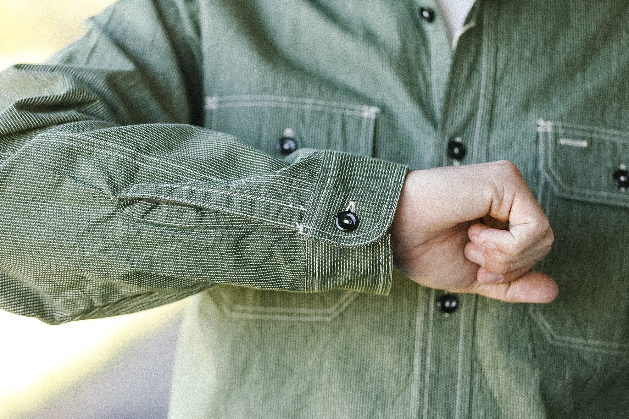 Person wearing a green corduroy shirt with rolled-up sleeves.