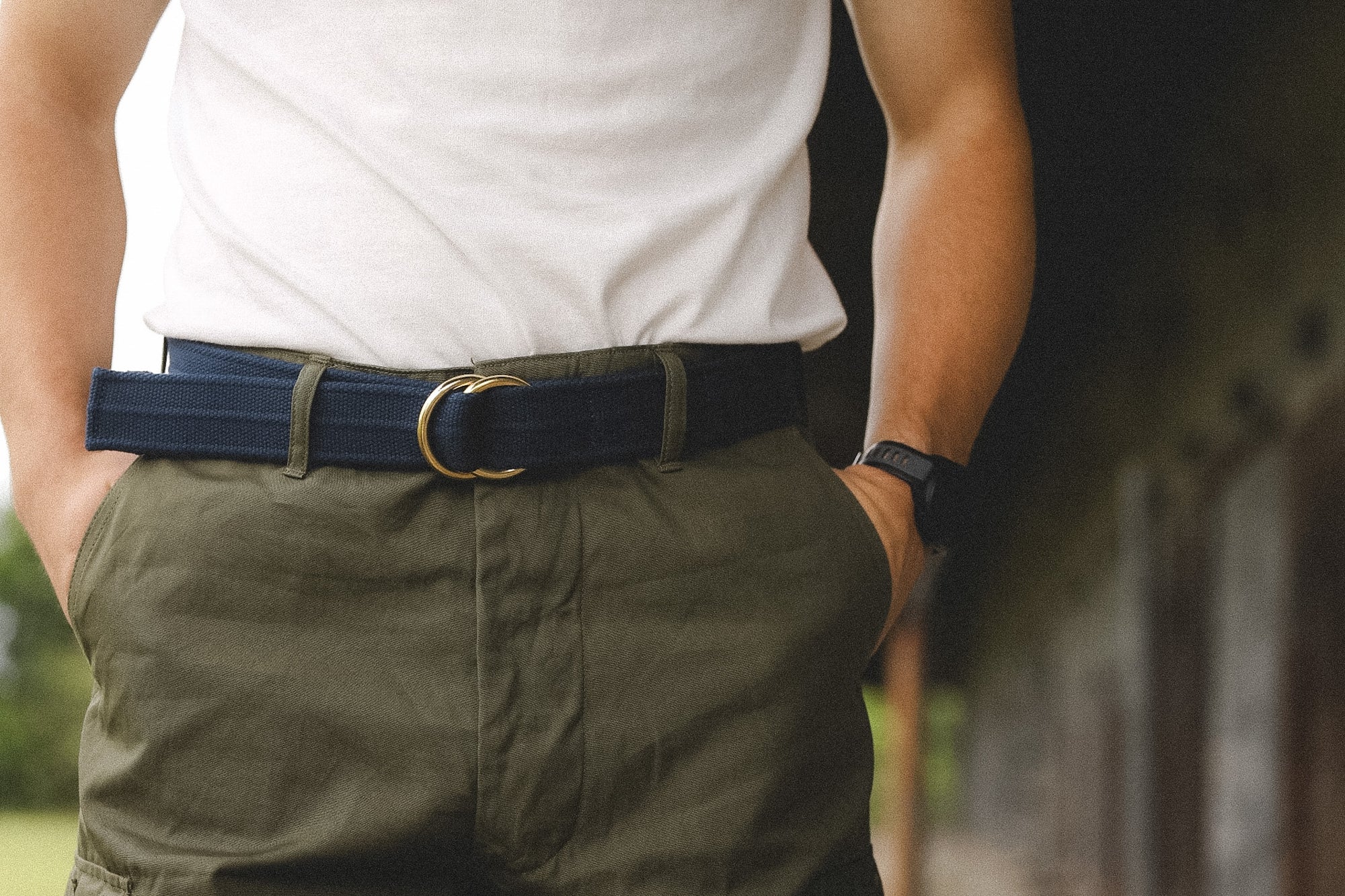 Person wearing a white shirt, green pants, and a blue belt with a gold buckle.