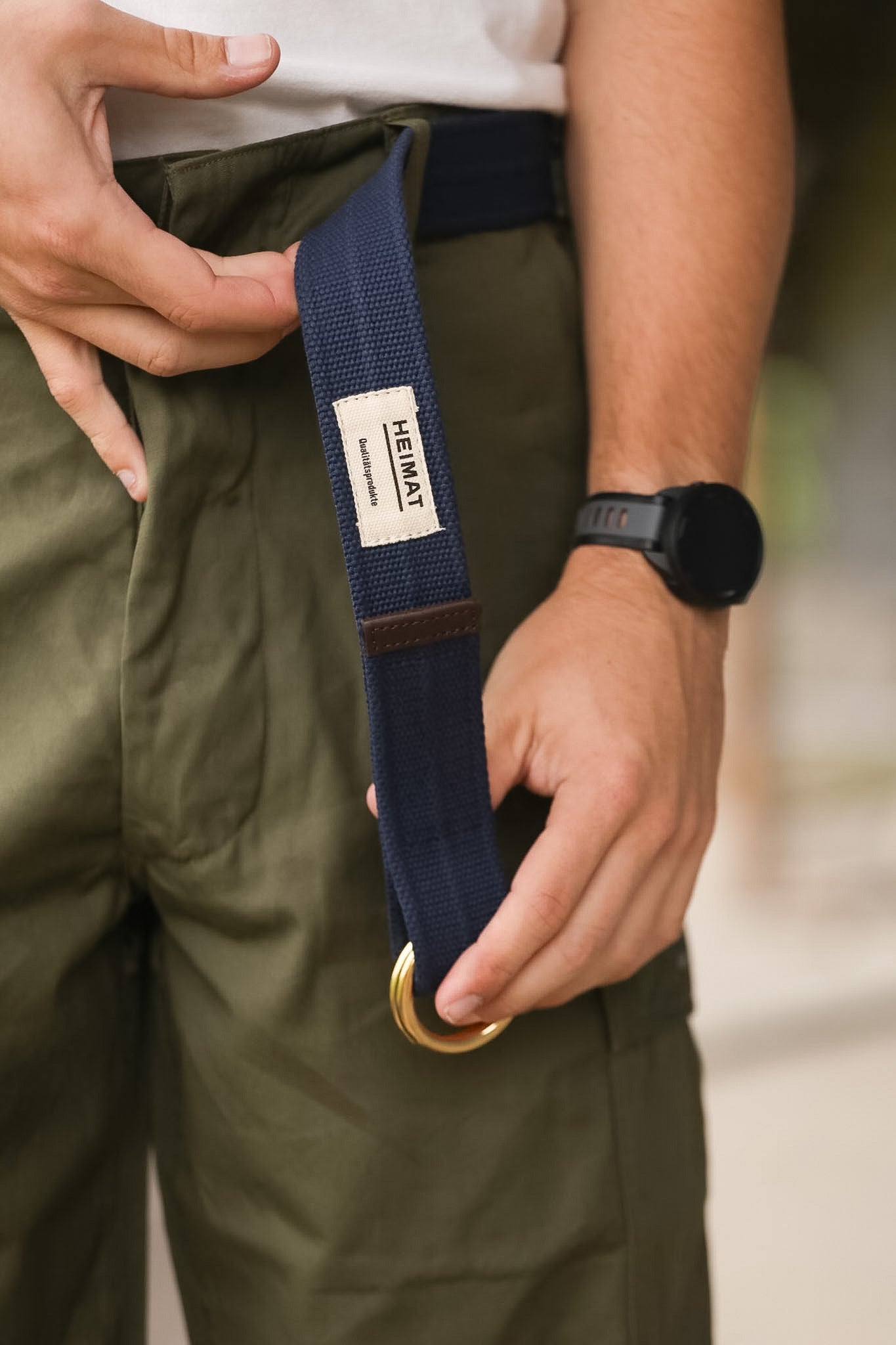 Person wearing a navy belt with a gold buckle, holding it with one hand.