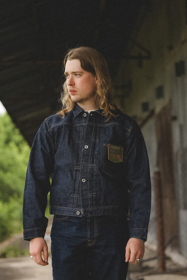 Man wearing a dark denim jacket standing outdoors with a blurred background