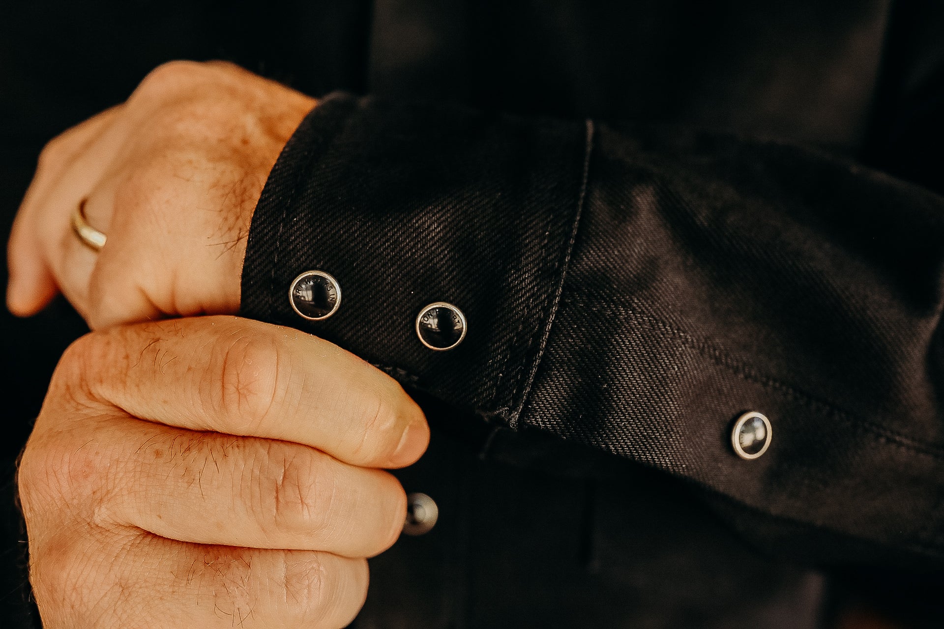 Close-up of hands adjusting black shirt cuff with metal snap buttons from Iron Shop Provisions