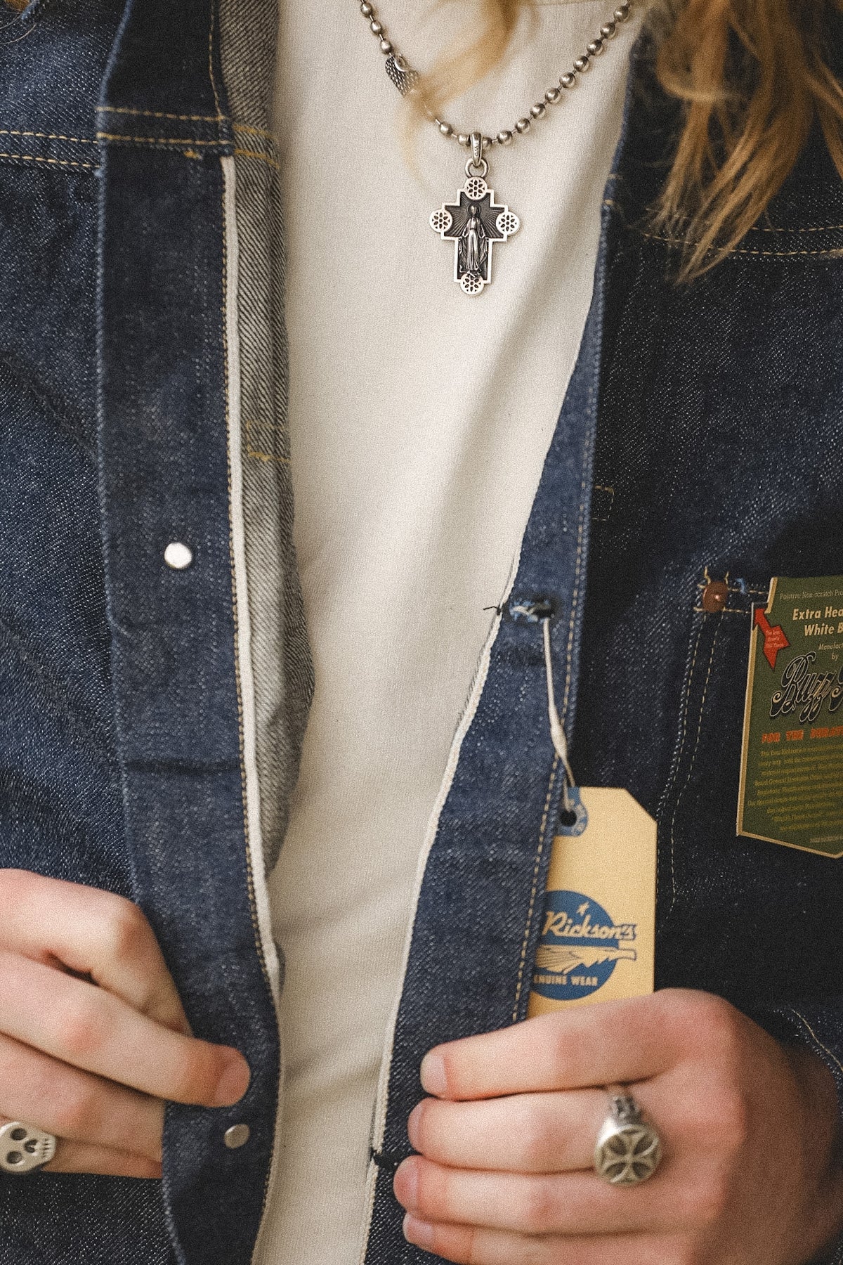 Person wearing a denim jacket with a visible brand tag, holding the jacket open.