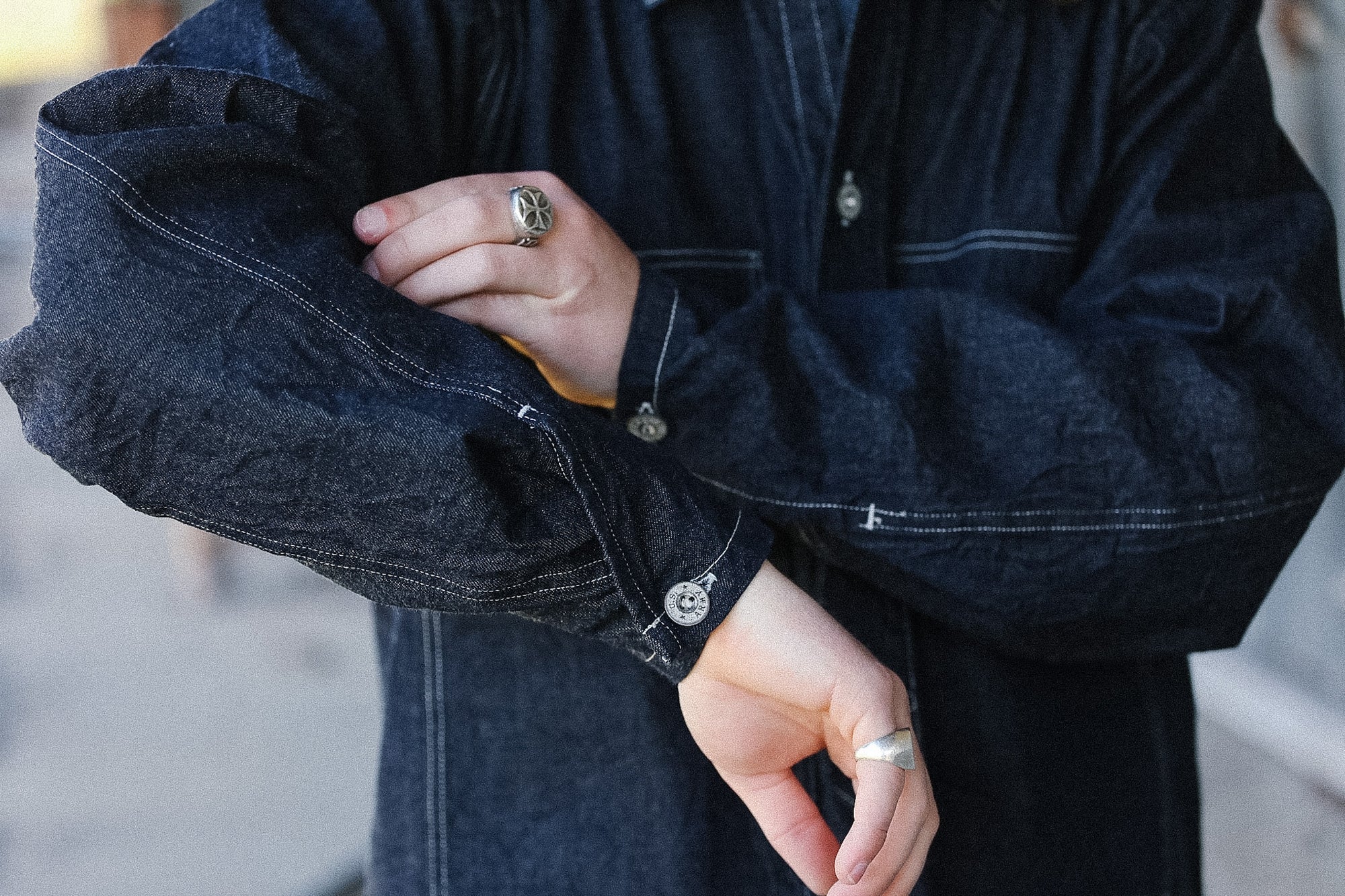 Person wearing a dark denim jacket with visible buttons and rings.