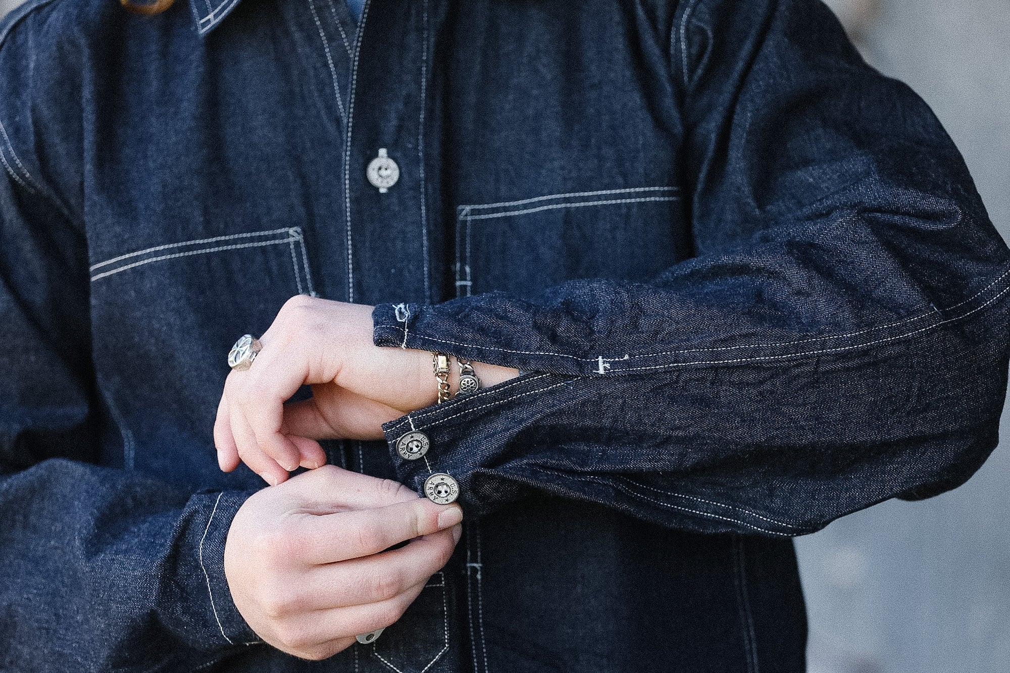 Person wearing a dark denim jacket with buttons being fastened.
