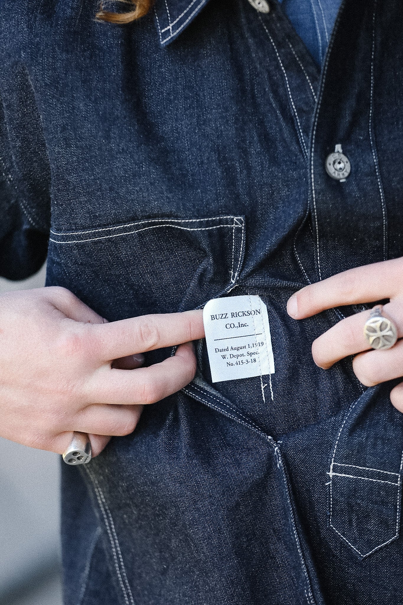 Close-up of a person holding a denim jacket with a brand label.