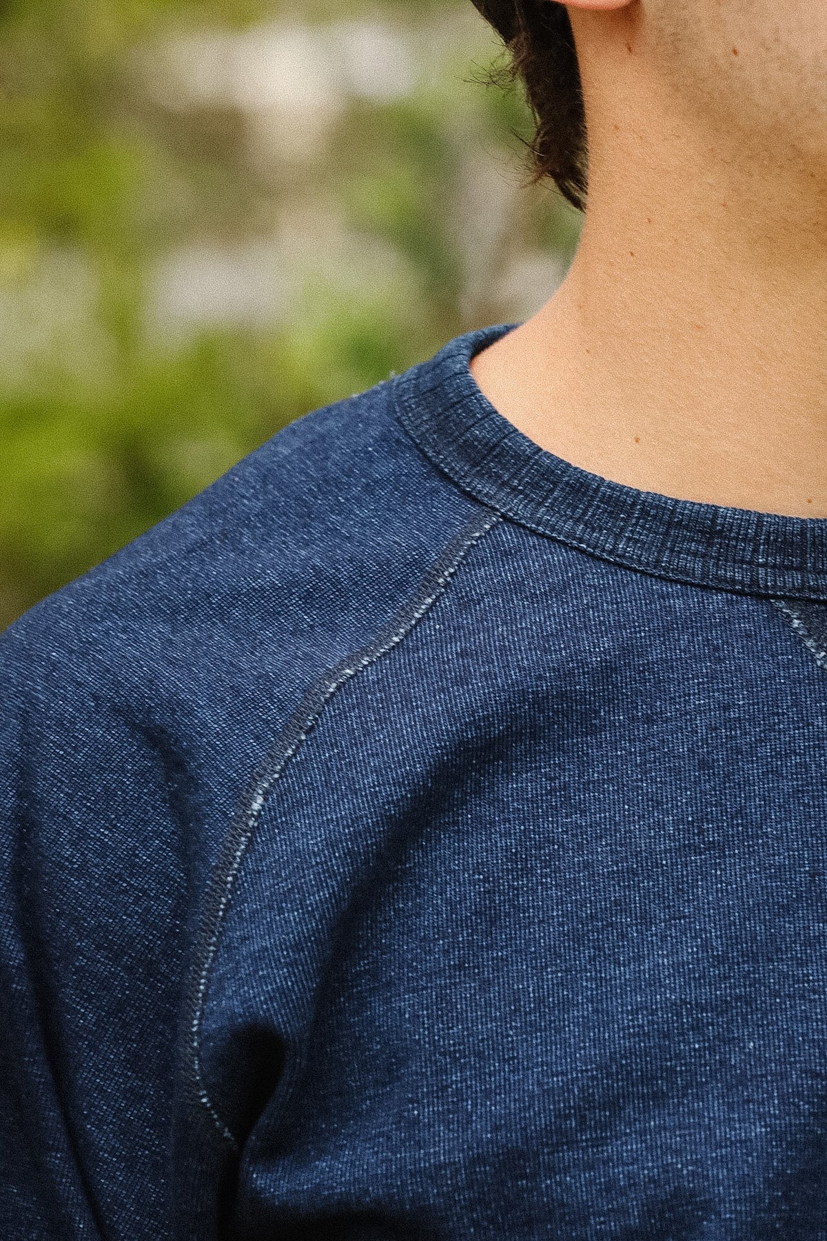 detail shot of a textured blue shirt with a green foliage background. 