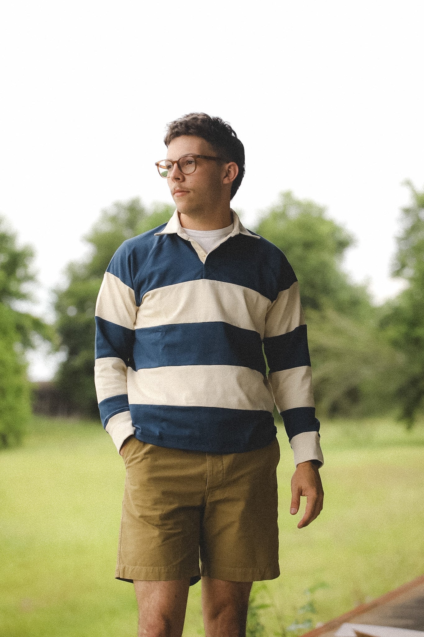 Man wearing a striped shirt and shorts standing outdoors with trees in the background