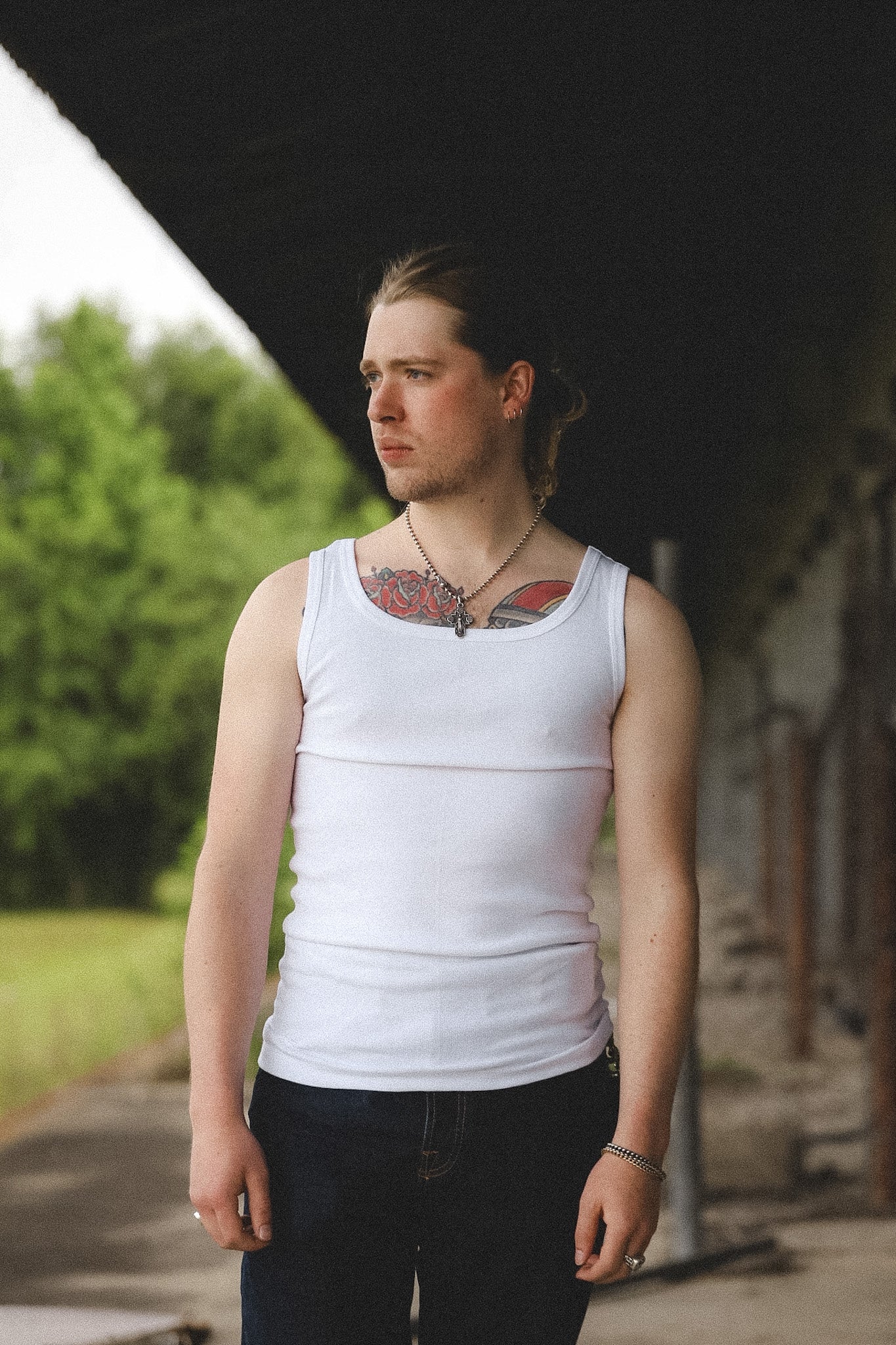 Person wearing a white tank top with tattoos visible, standing outdoors.