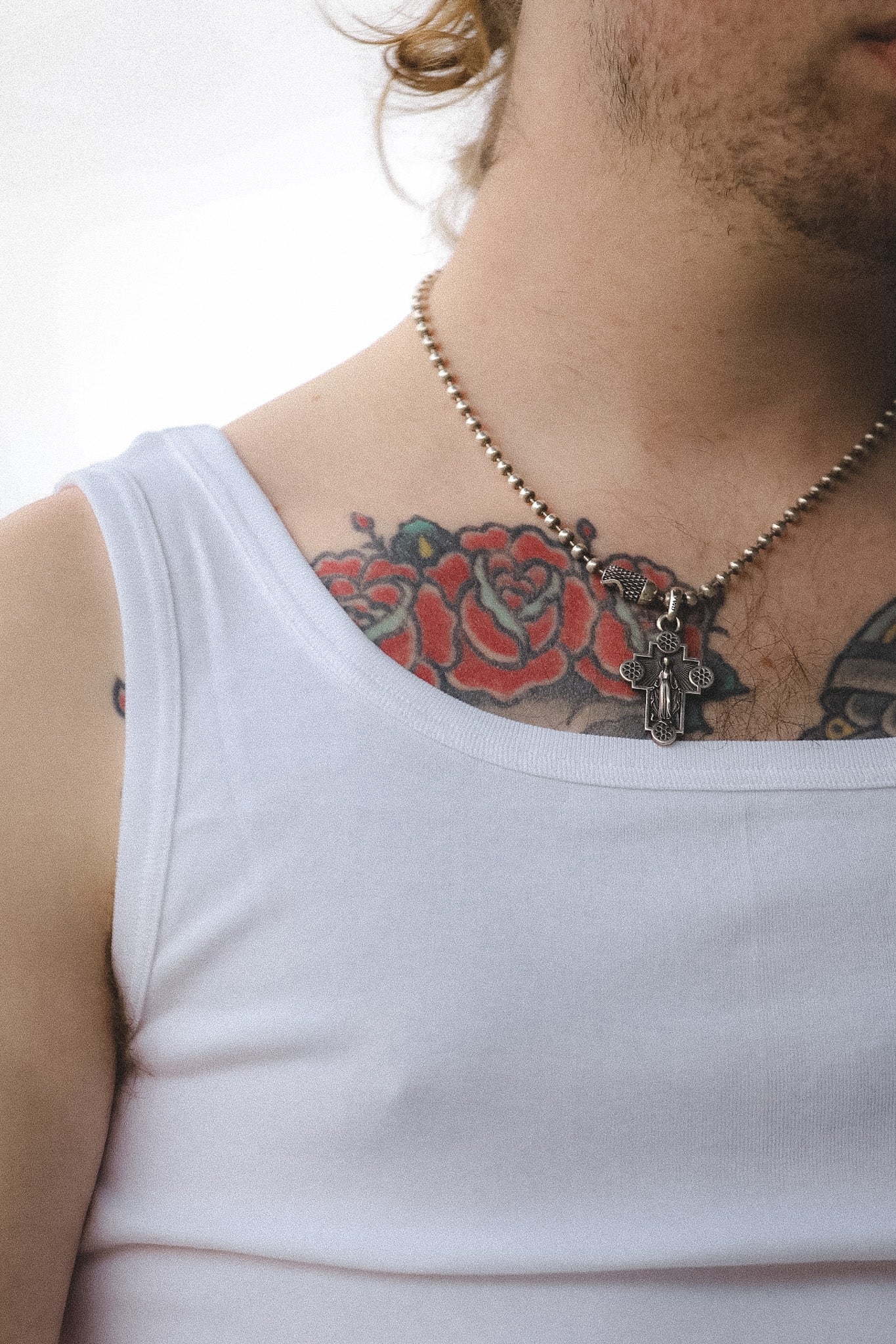 Person wearing a white tank top with visible tattoos on the neck and shoulder, wearing a necklace.
