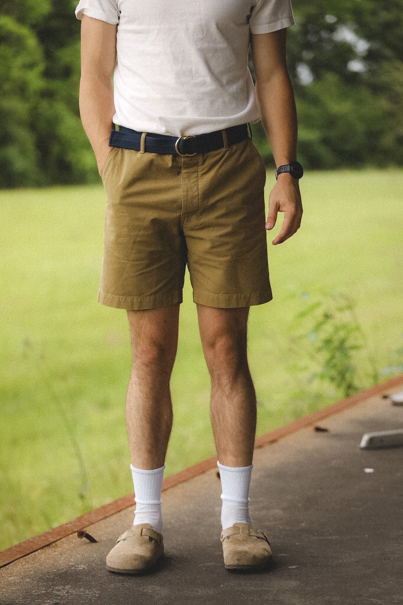 Person wearing a white shirt, khaki shorts, and beige shoes with a blurred green background