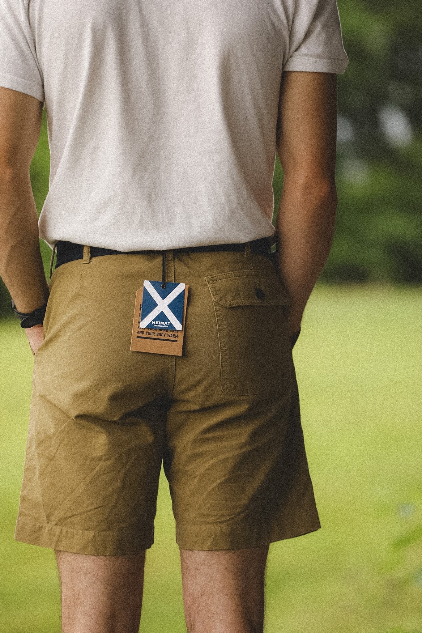Person wearing brown shorts with a visible brand tag in an outdoor setting