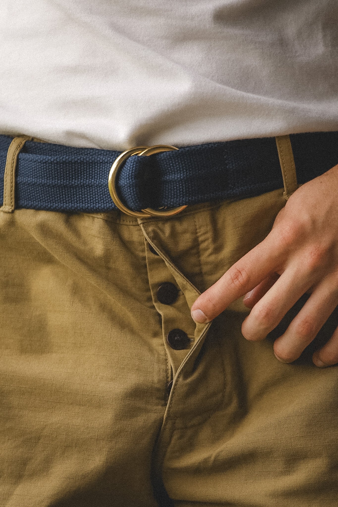 Close-up of a person wearing brown pants with a navy belt and white shirt.