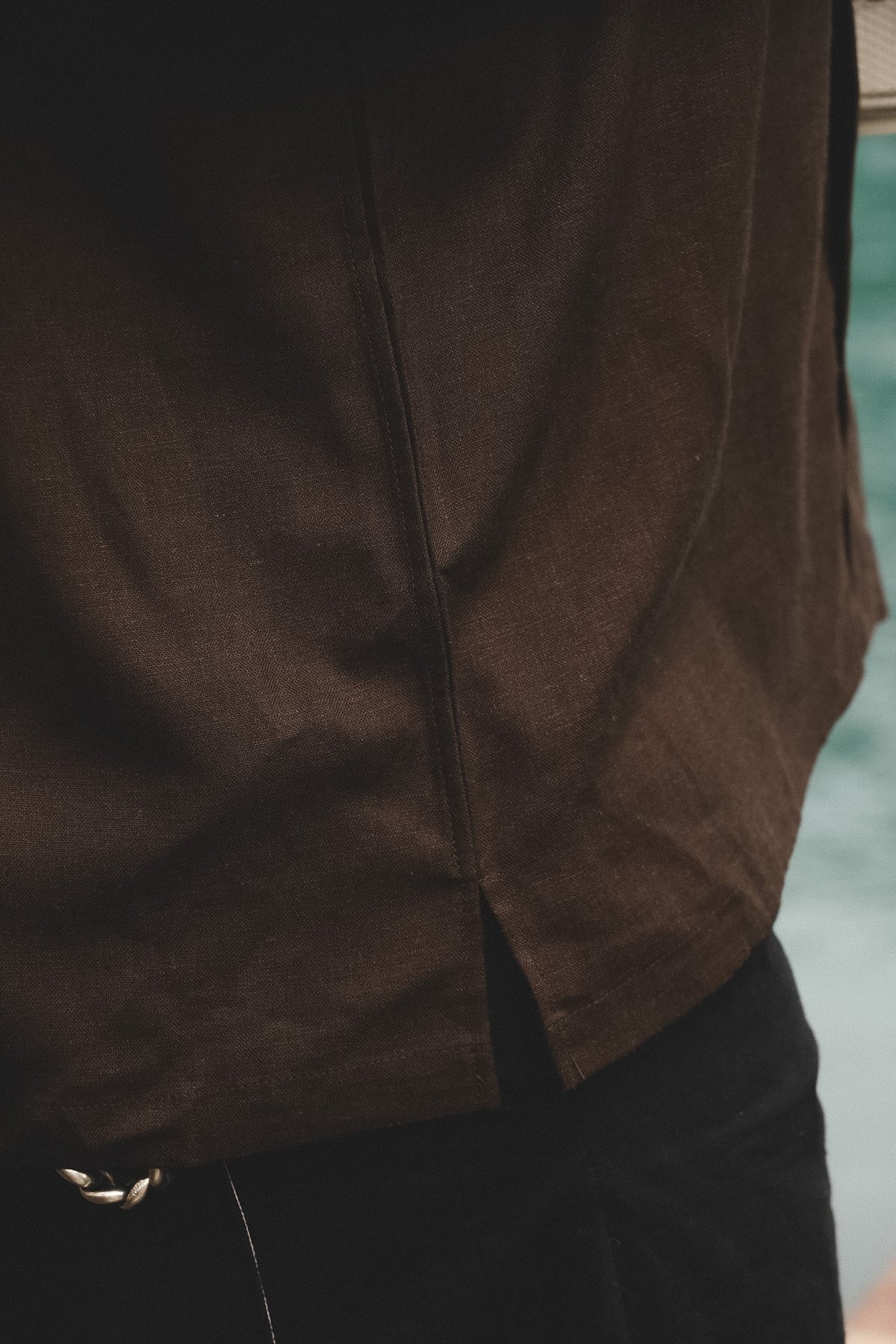 Close-up of a person wearing a dark brown textured shirt and black pants, with a blurred outdoor background.
