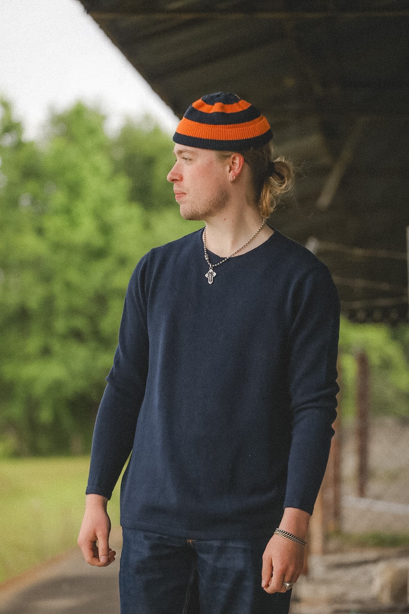 Person wearing a navy sweater and striped beanie outdoors with greenery in the background