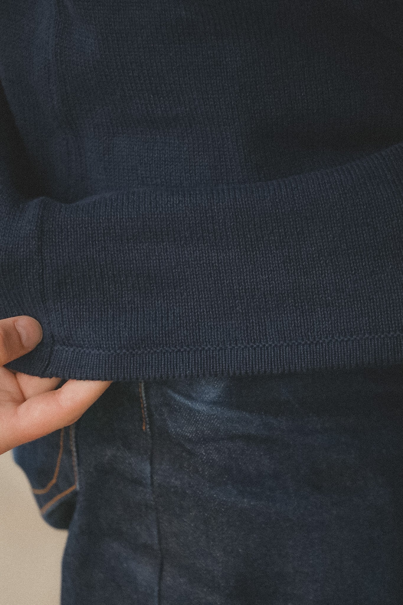 Close-up of a navy blue sweater sleeve with a hand holding it, on a neutral background.