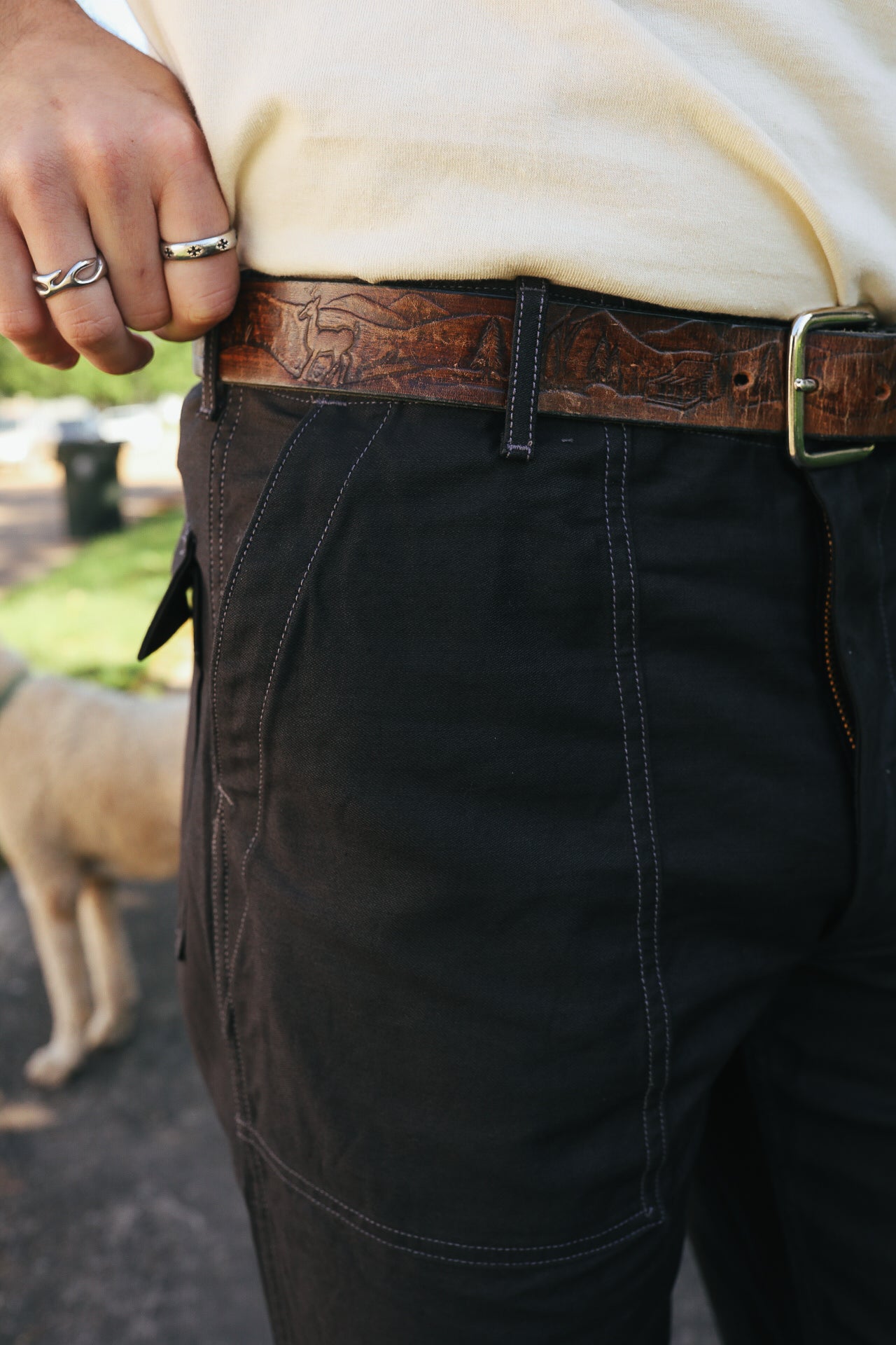 Close-up of person wearing dark pants and a leather belt with engraved mountain and deer design
