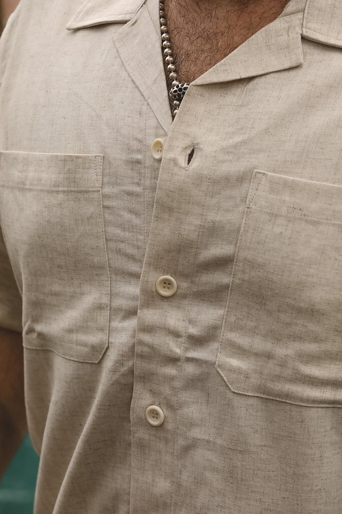 Close-up of a man wearing a light beige linen short-sleeve button-up shirt with two chest pockets and cream-colored buttons.