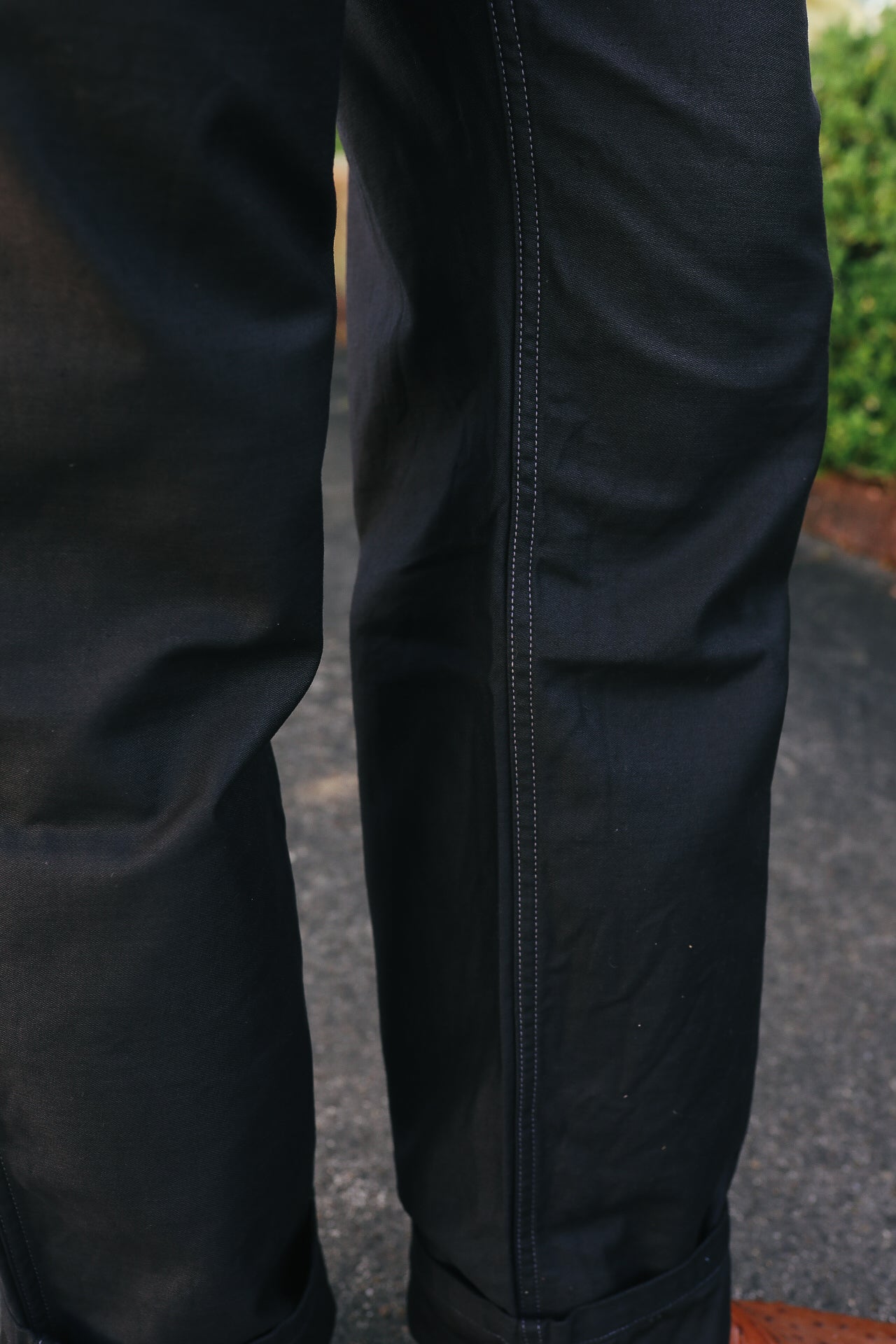 Close-up of black durable work pants with reinforced stitching, worn outdoors on pavement