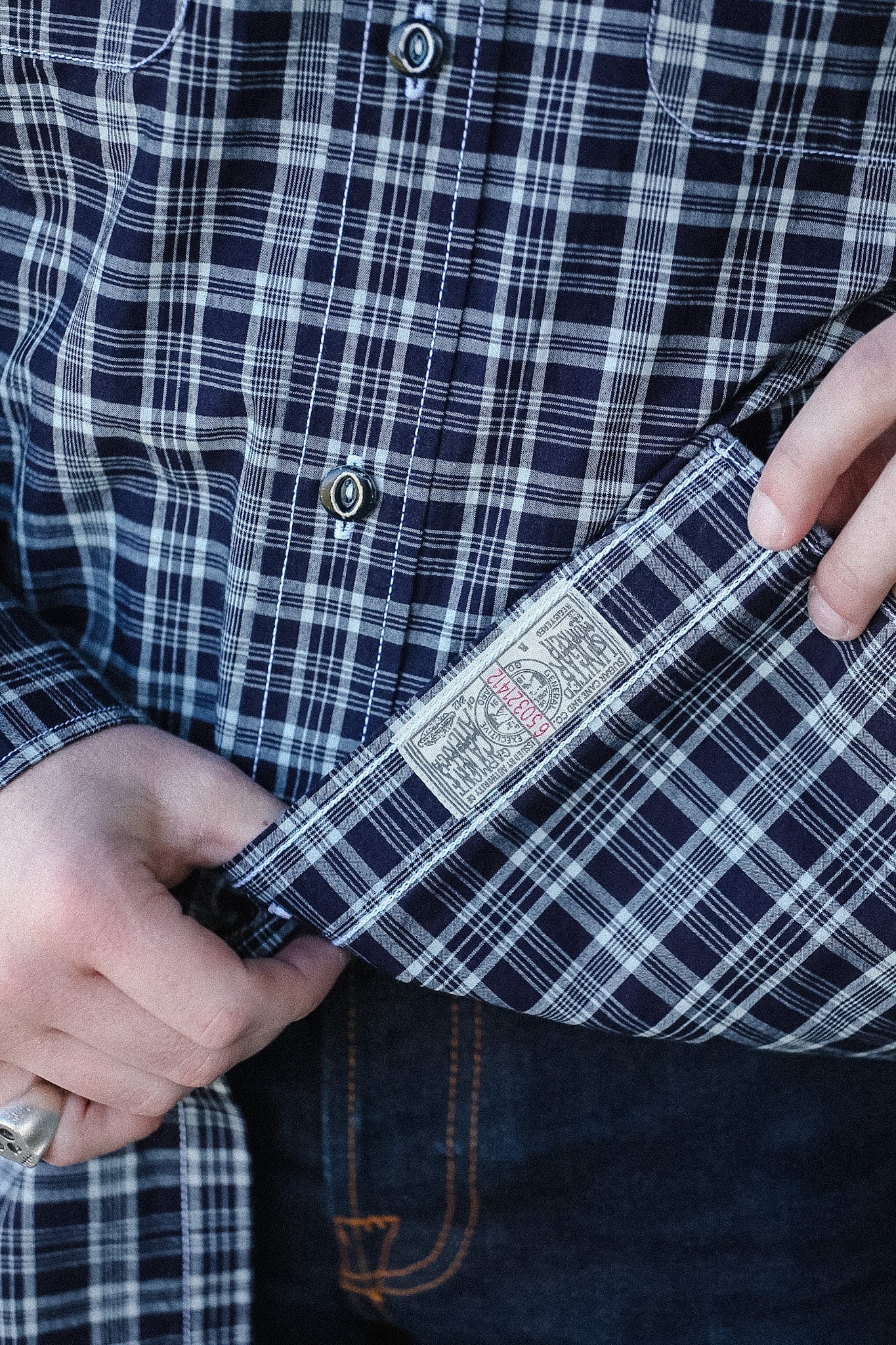 Close-up of a person wearing a plaid shirt with a visible brand label.