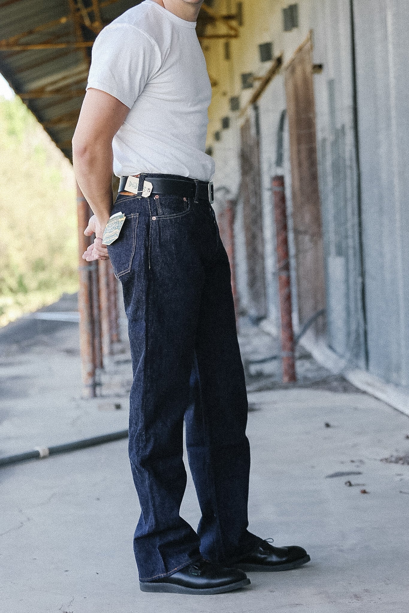 Person wearing dark blue jeans and a white shirt standing on a sidewalk.