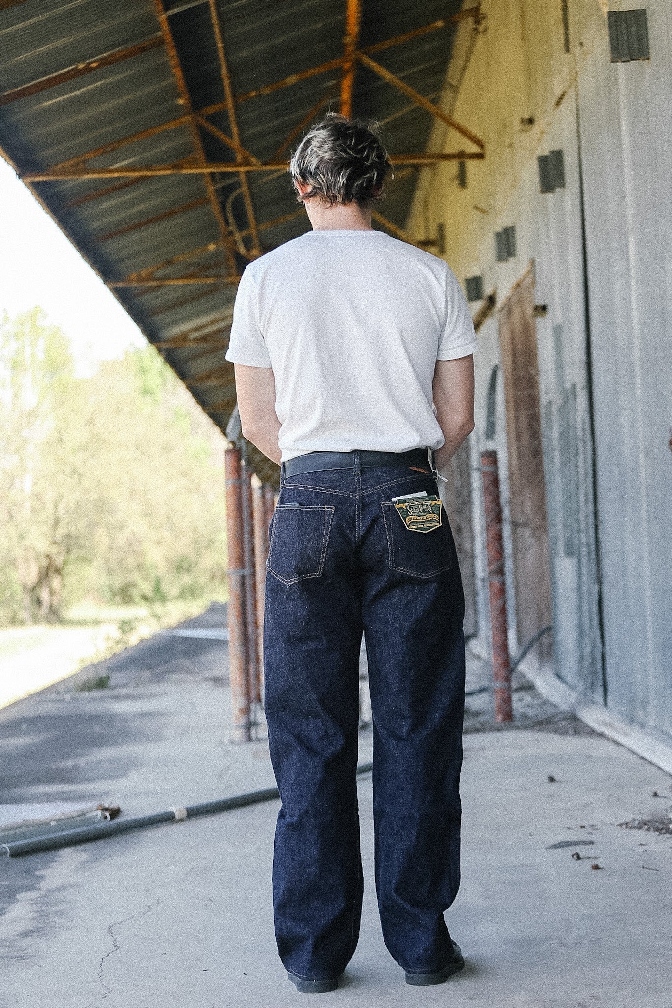 Person wearing a white t-shirt and blue jeans standing under a metal roof.
