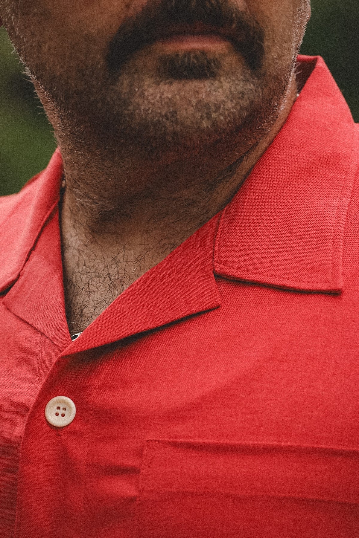 Close-up of a man wearing a red short-sleeve collared button-up shirt, showing the collar, chest pocket, and a white button.