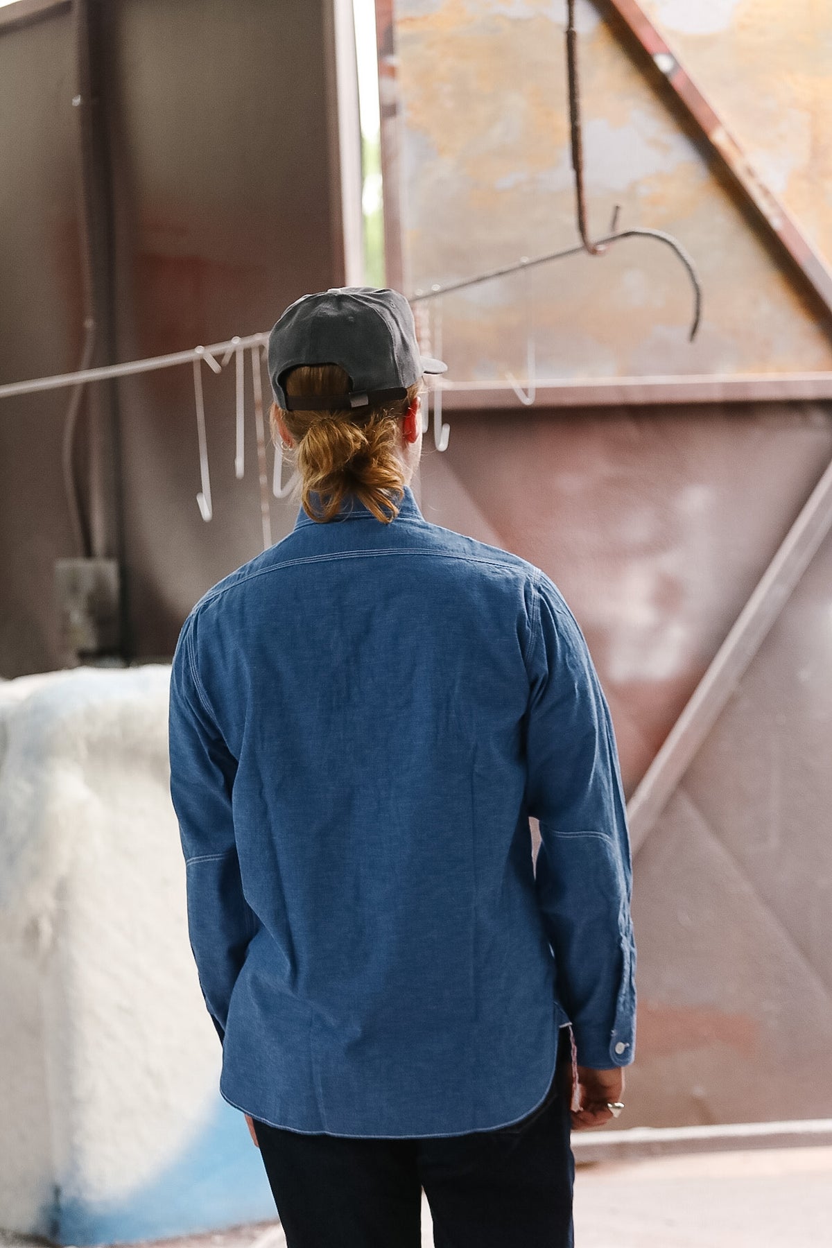 Person wearing a blue shirt and black cap standing in front of a textured wall.