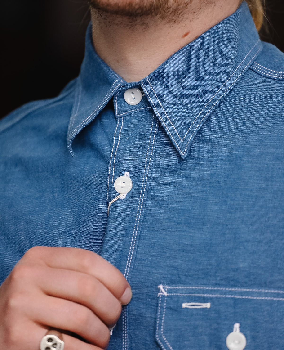 Close-up of a person wearing a blue denim shirt with white stitching details.