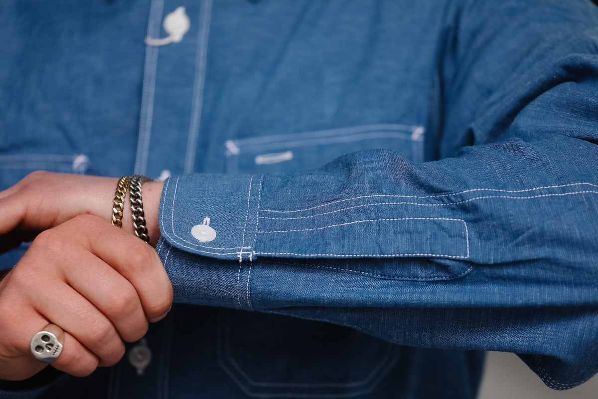 Close-up of a person wearing a blue denim shirt with rolled-up sleeves, focusing on the cuff.