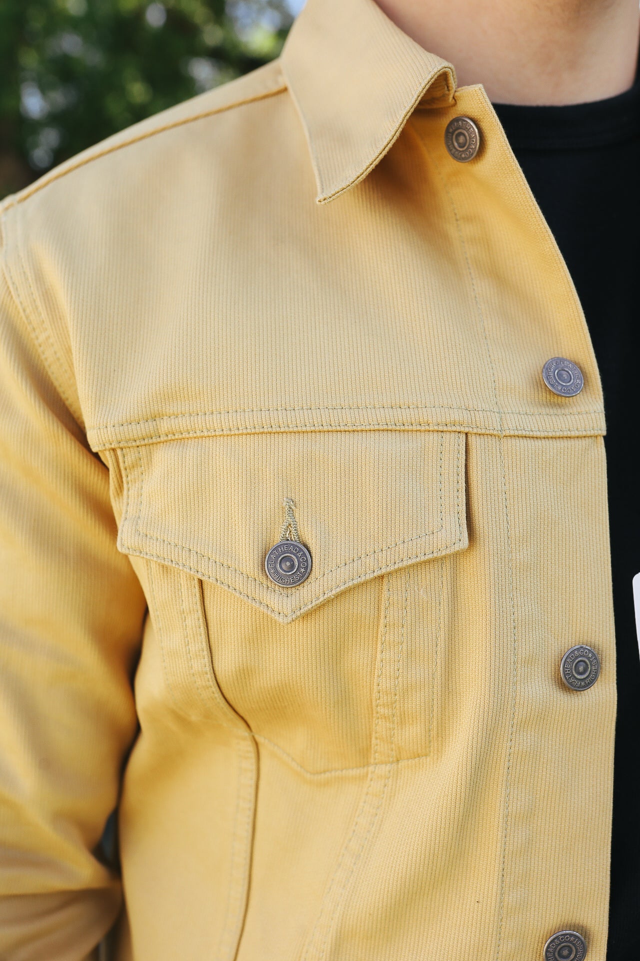 Close-up of a yellow work jacket with metal snaps and chest pocket over a black shirt outdoors