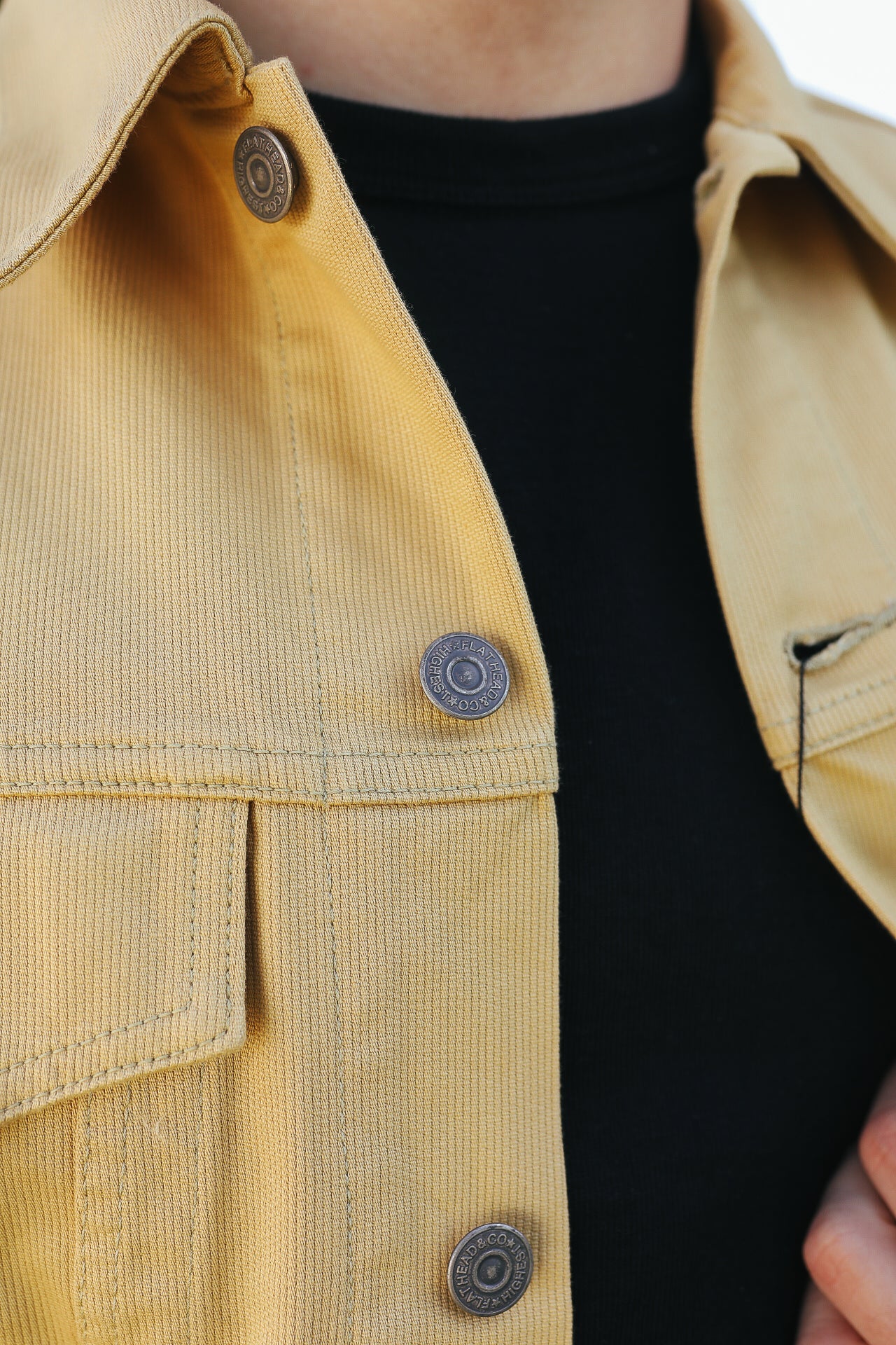 Close-up of yellow work jacket with metal snap buttons over a black shirt
