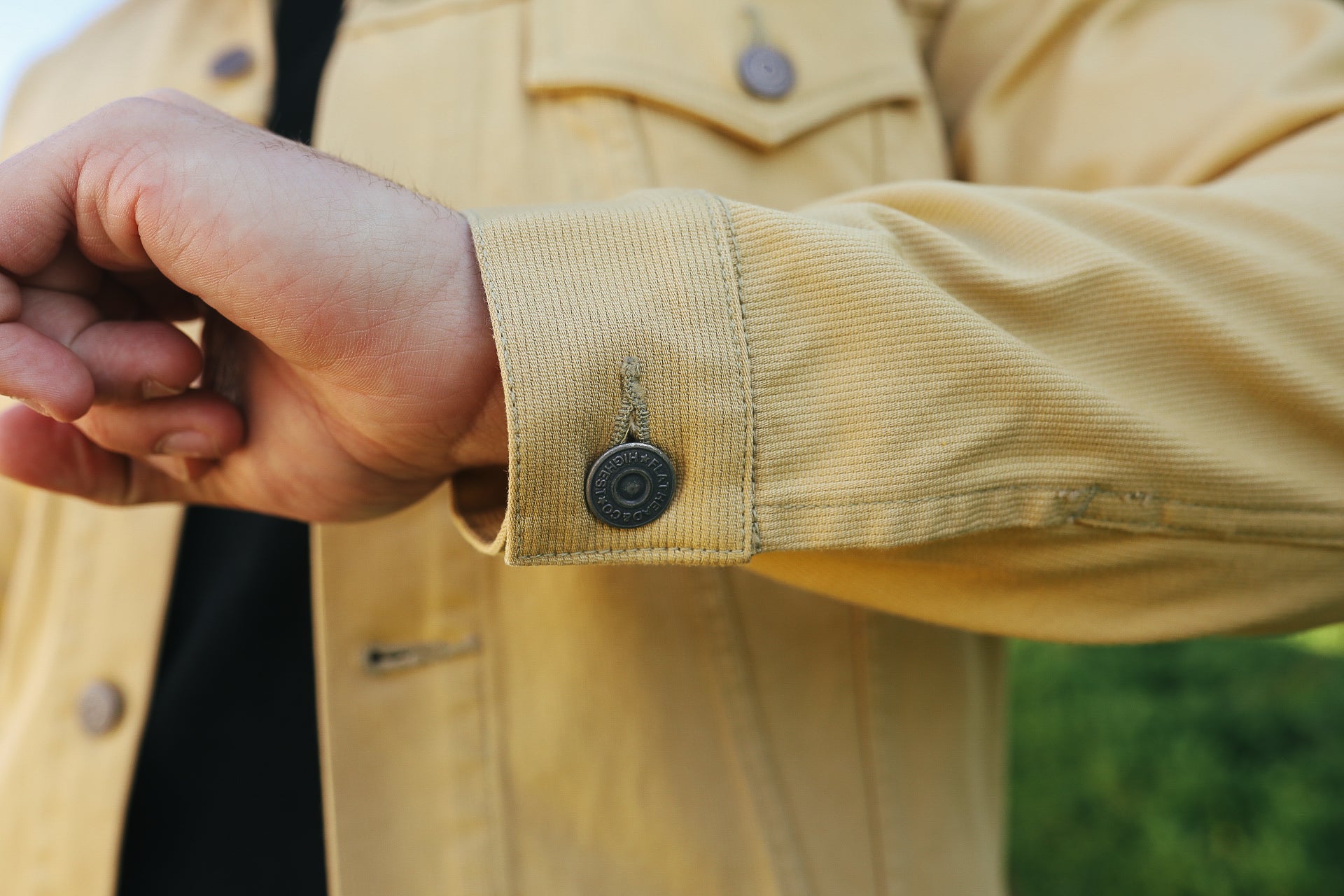 Close-up of a tan work jacket cuff with a branded metal button, worn over a black shirt