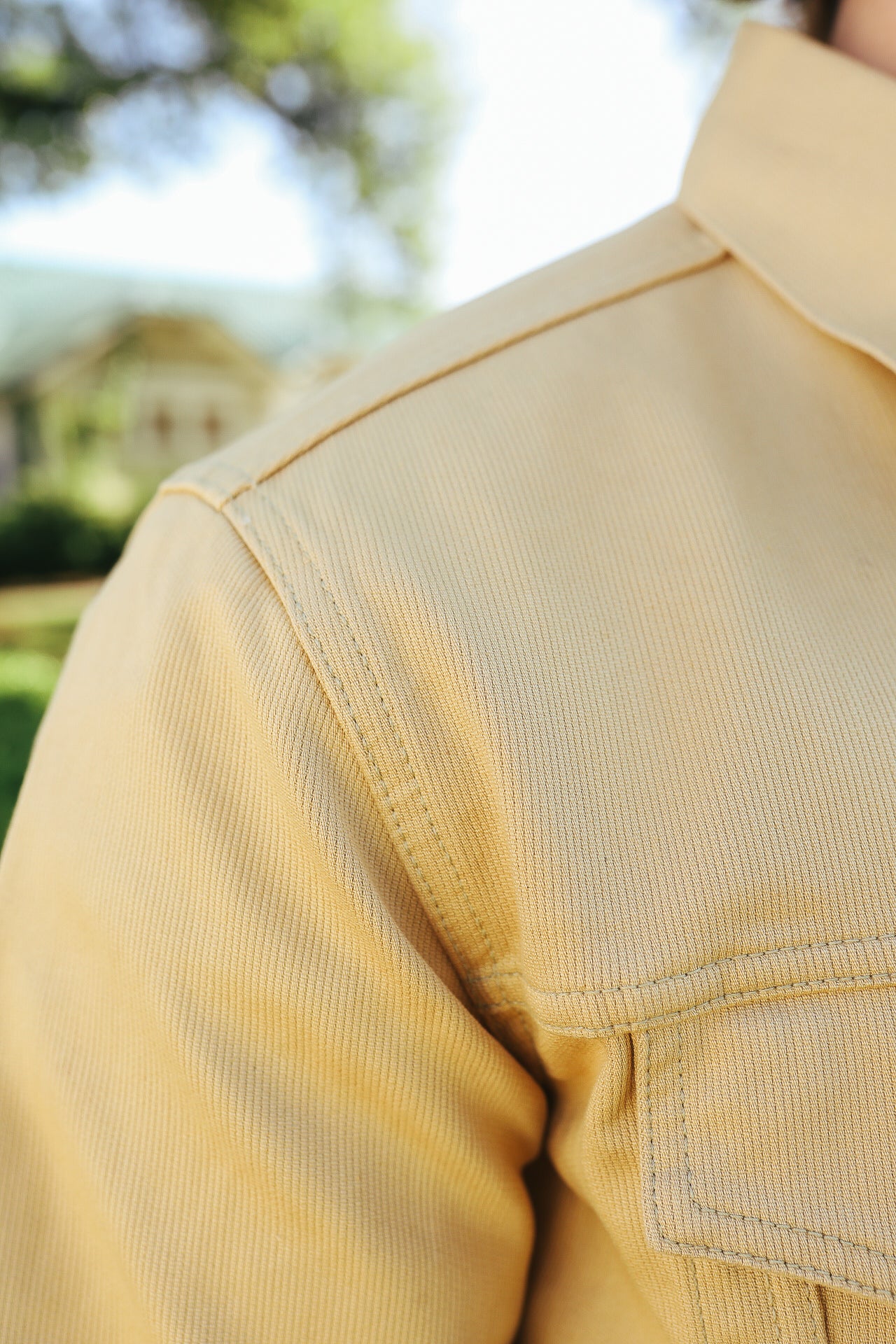 Close-up of yellow durable fabric shirt shoulder with visible stitching, outdoor background