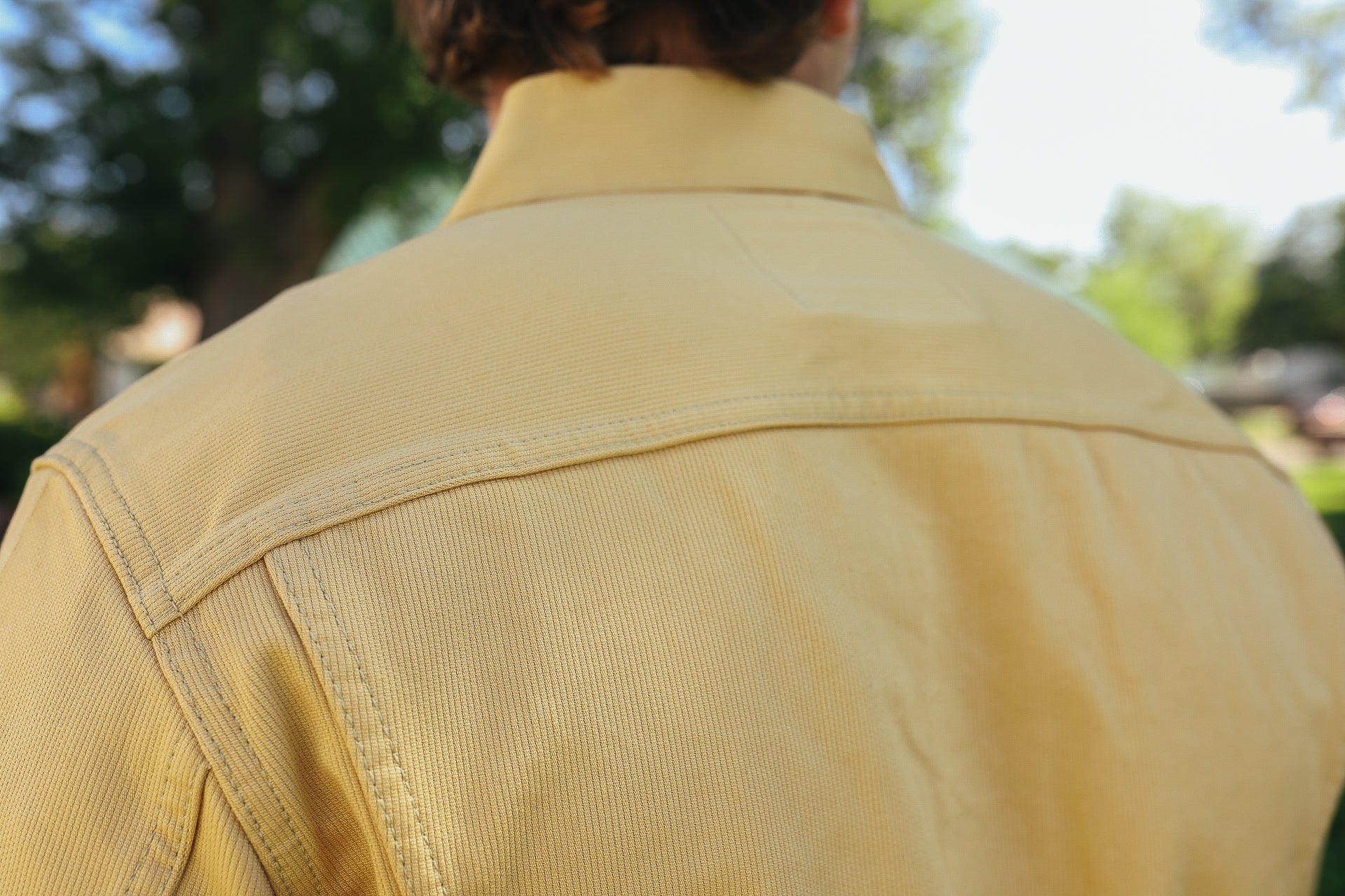 Close-up of a person wearing a yellow work shirt outdoors with green trees in the background